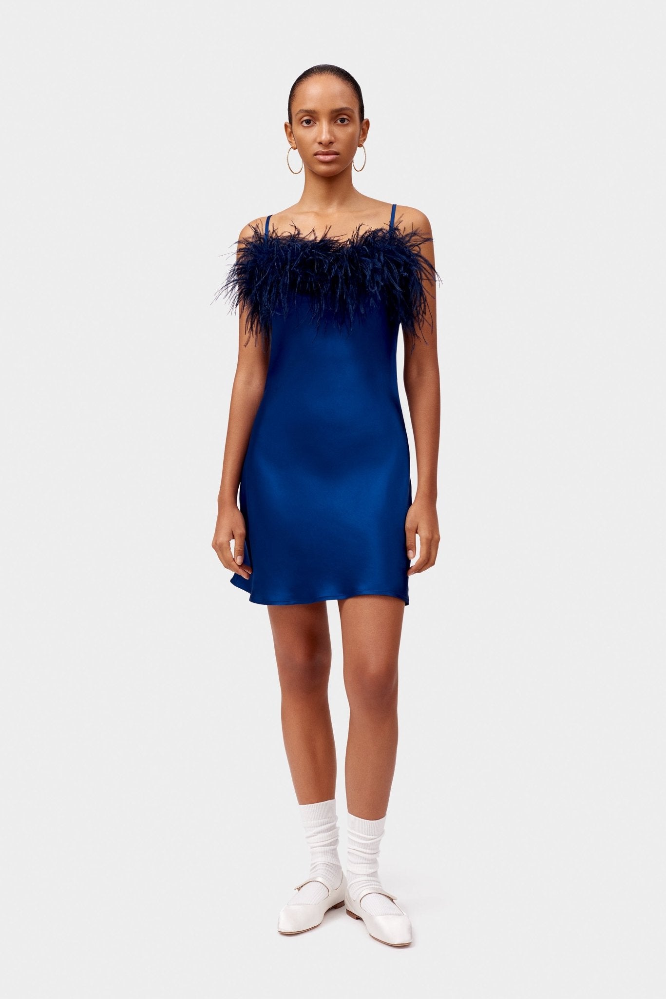 Woman wearing a mini navy satin slip dress with feathers.