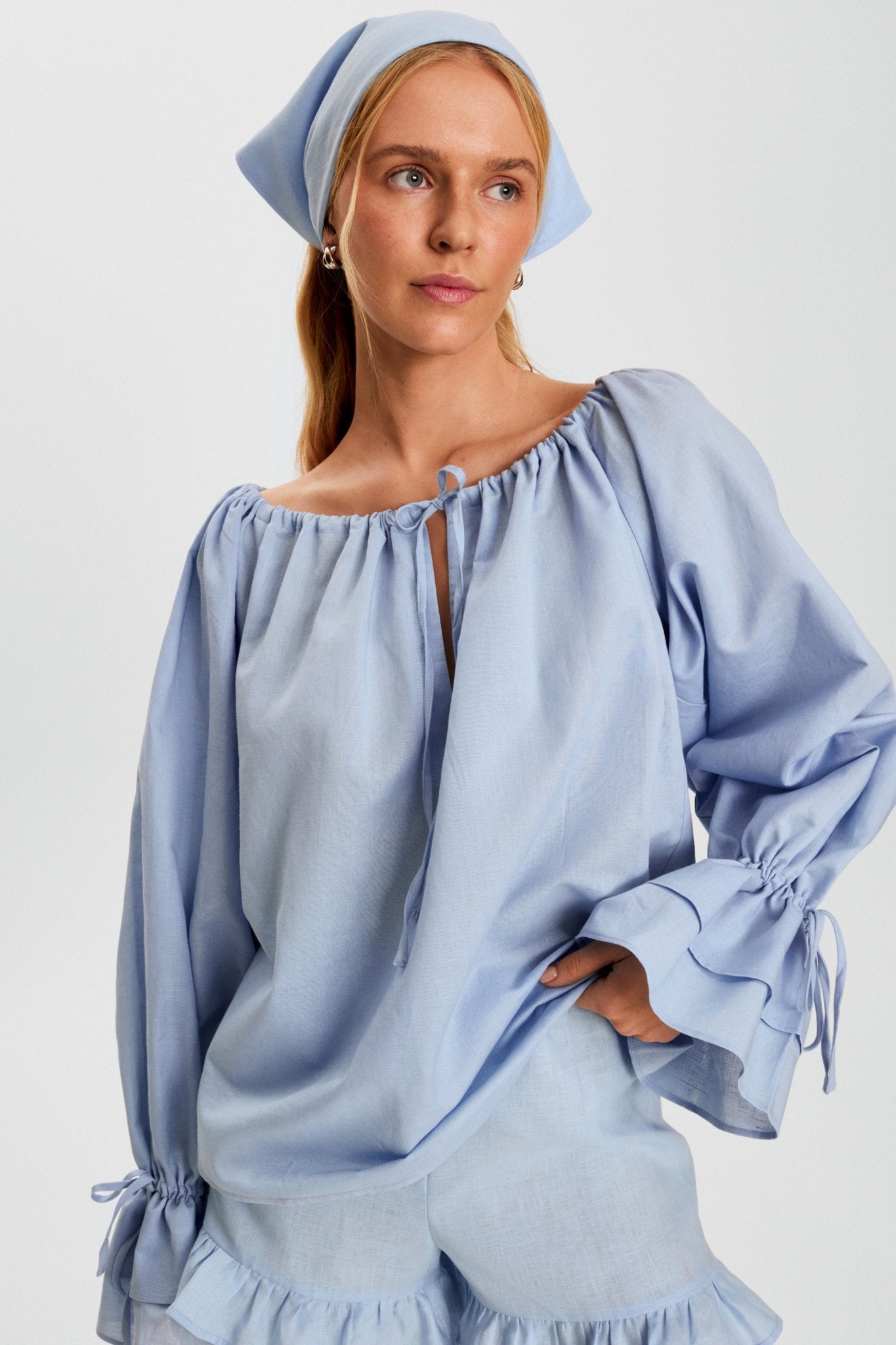 woman-wearing-a-linen-blue-blouse-with-long-sleeves-and-adjustable-round-neck-with-ties-and-blue-shorts-with-ruffles-and-matching-headscarf