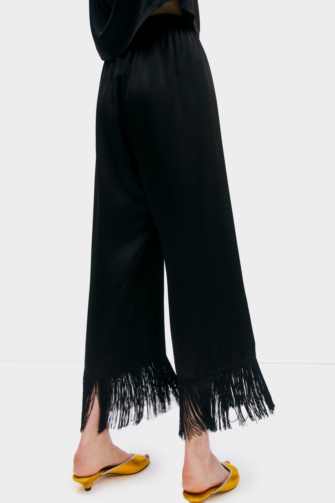 Close up of a person wearing black shirt and pants with fringed cuff and yellow sandals - ANNIE.G