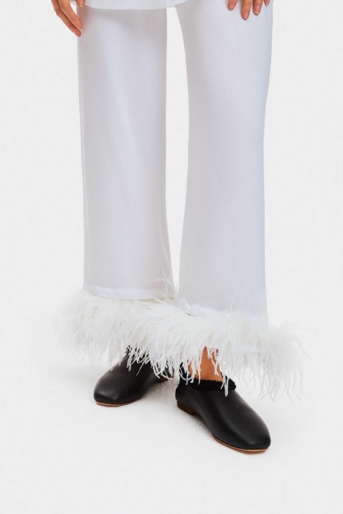 Person wearing white pyjamas pants with Double Feathers and black flat shoes.