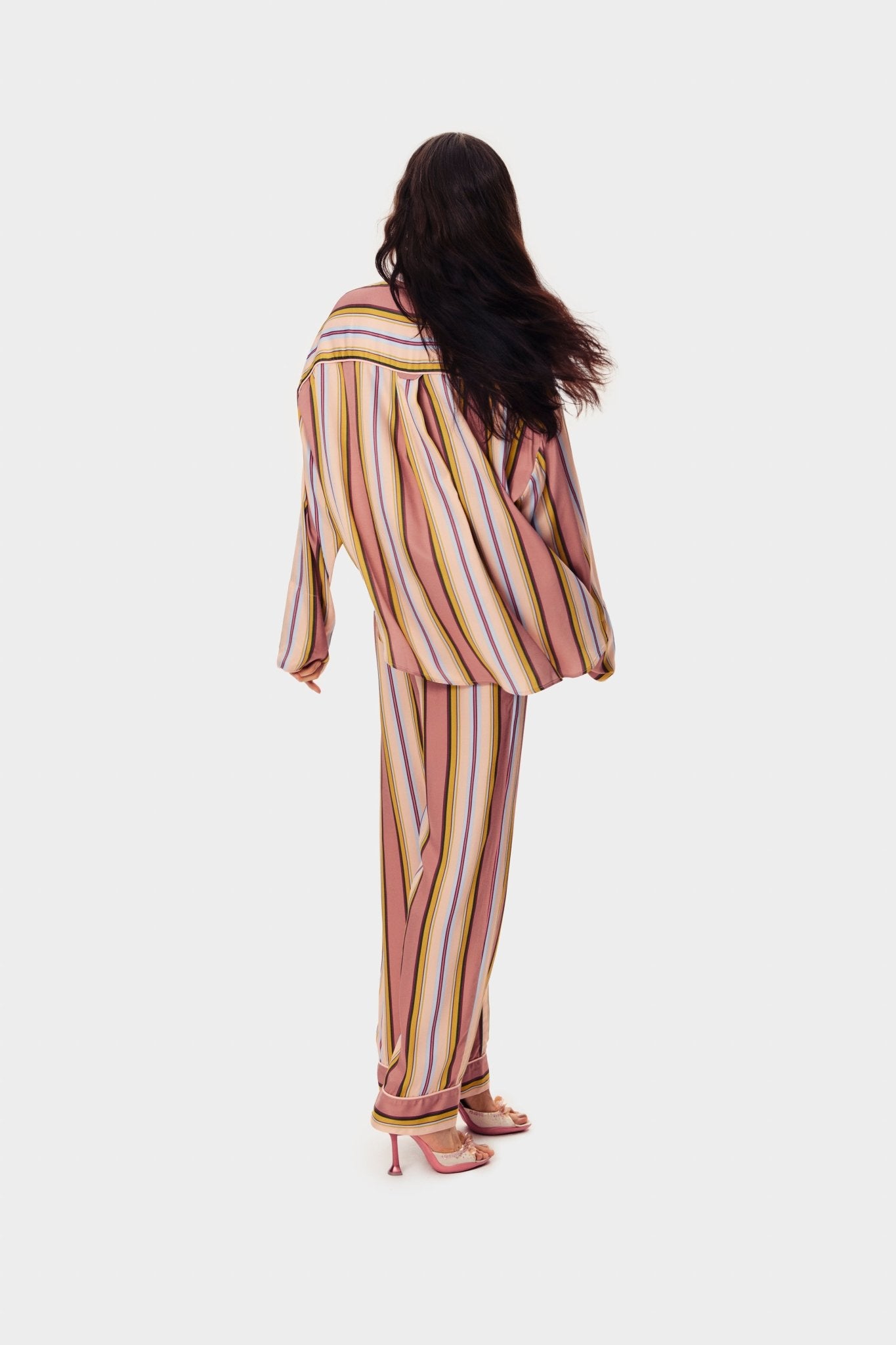 Woman wearing pink striped shirt and long pants with heels facing backwards.