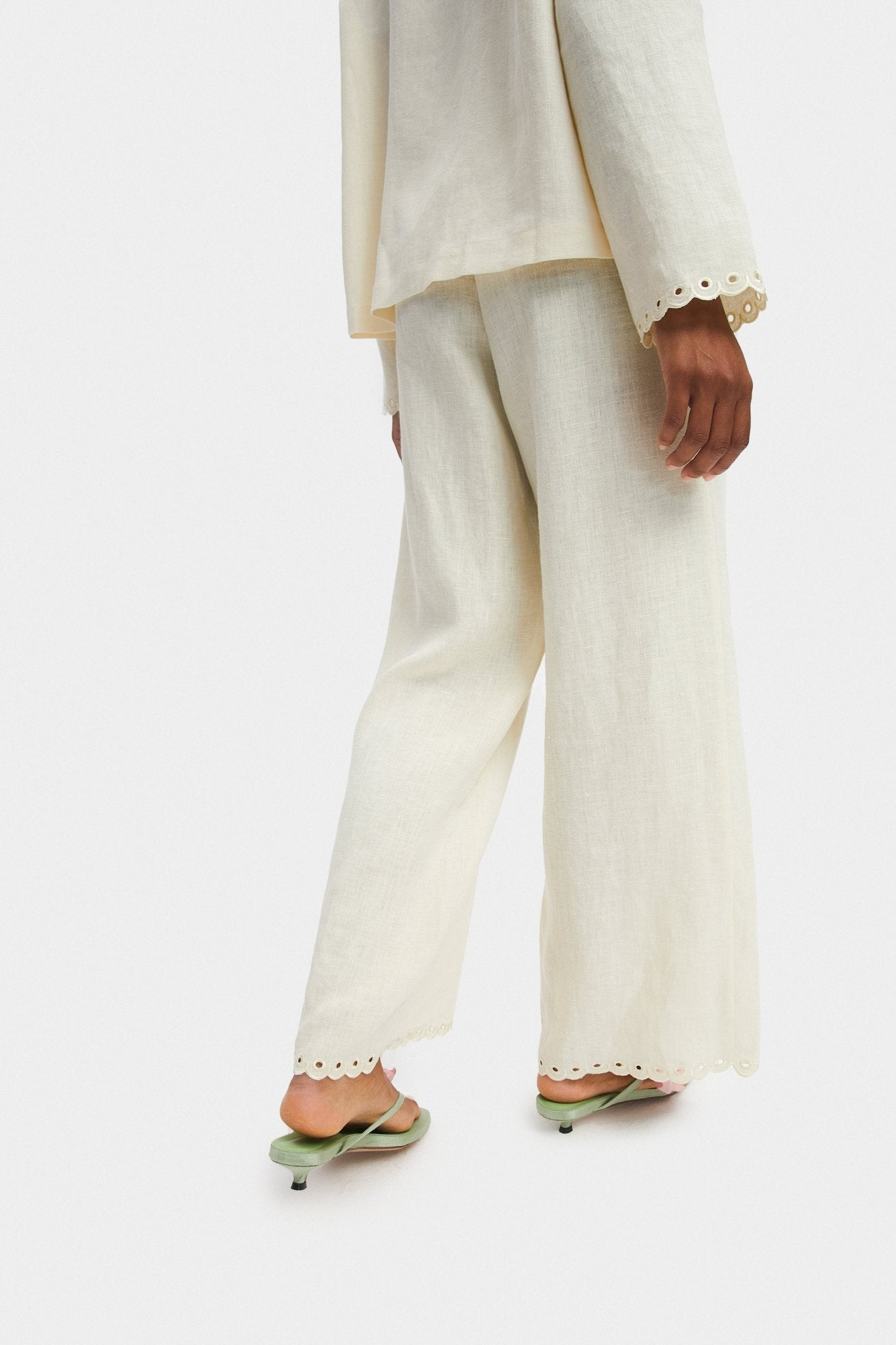 Person wearing cream pants with scalloped embroidered hem and green shoes.