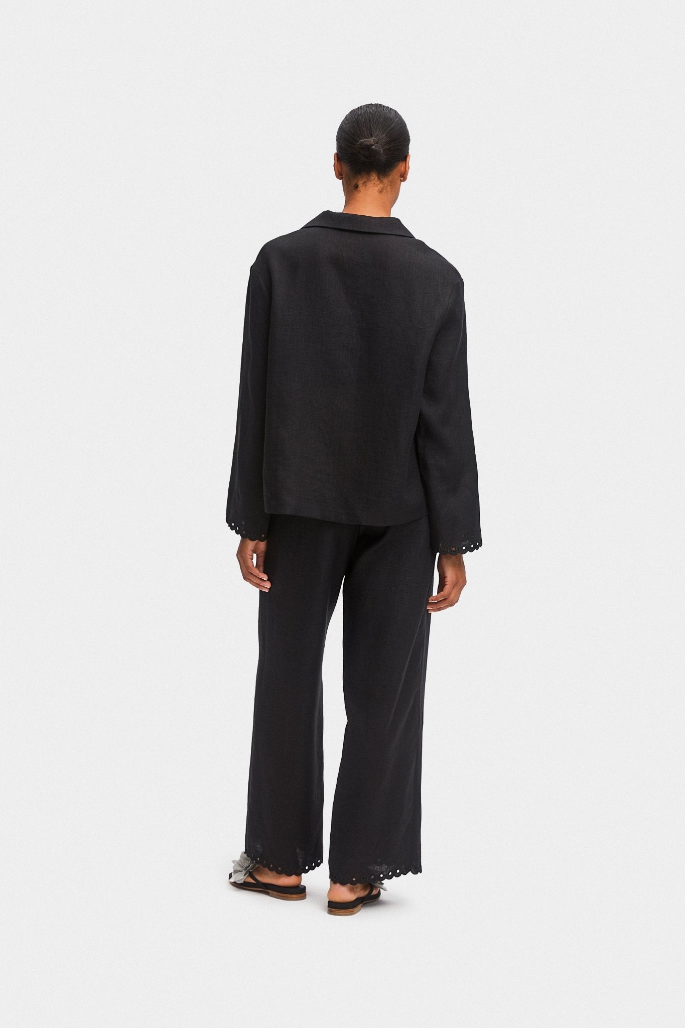 Person wearing black shirt and pants with scalloped embroidered hem and black shoes.