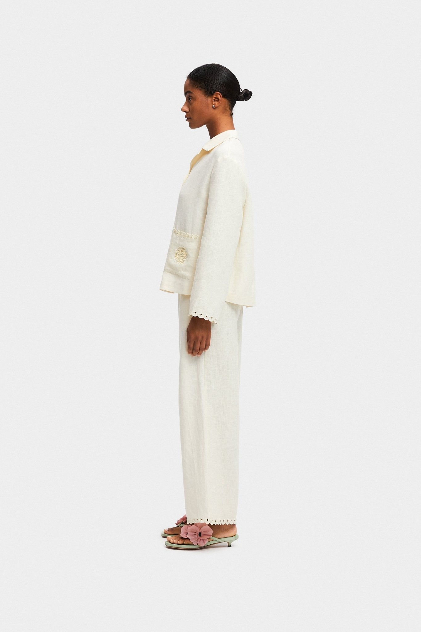 Woman standing on the side wearing cream pants and shirt and green shoes.