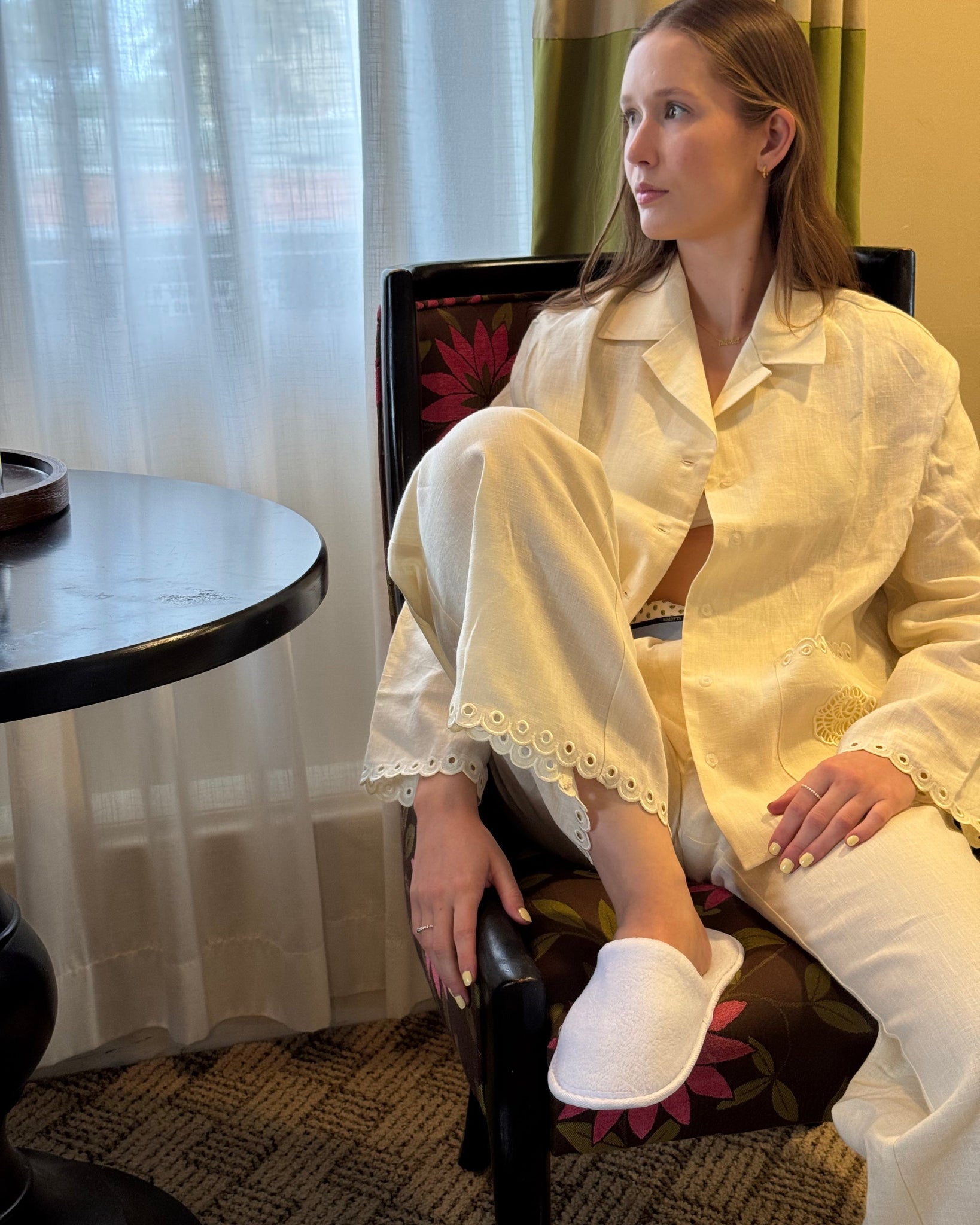 Woman in a cream pyjama shirt and pants set sitting on a chair with a patterned cushion.