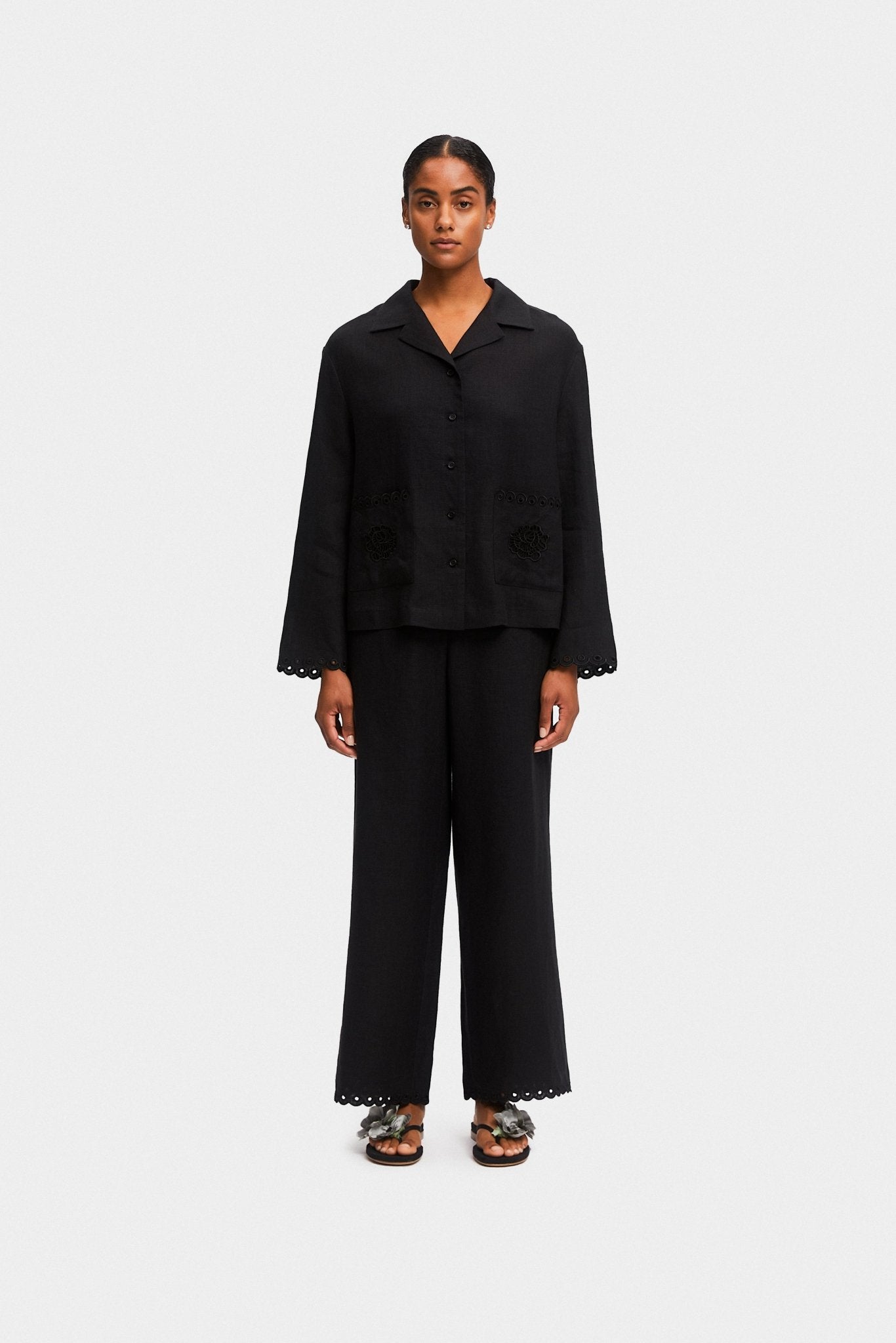 Woman wearing a black long sleeve shirt with scallop hem on sleeves and long pants.