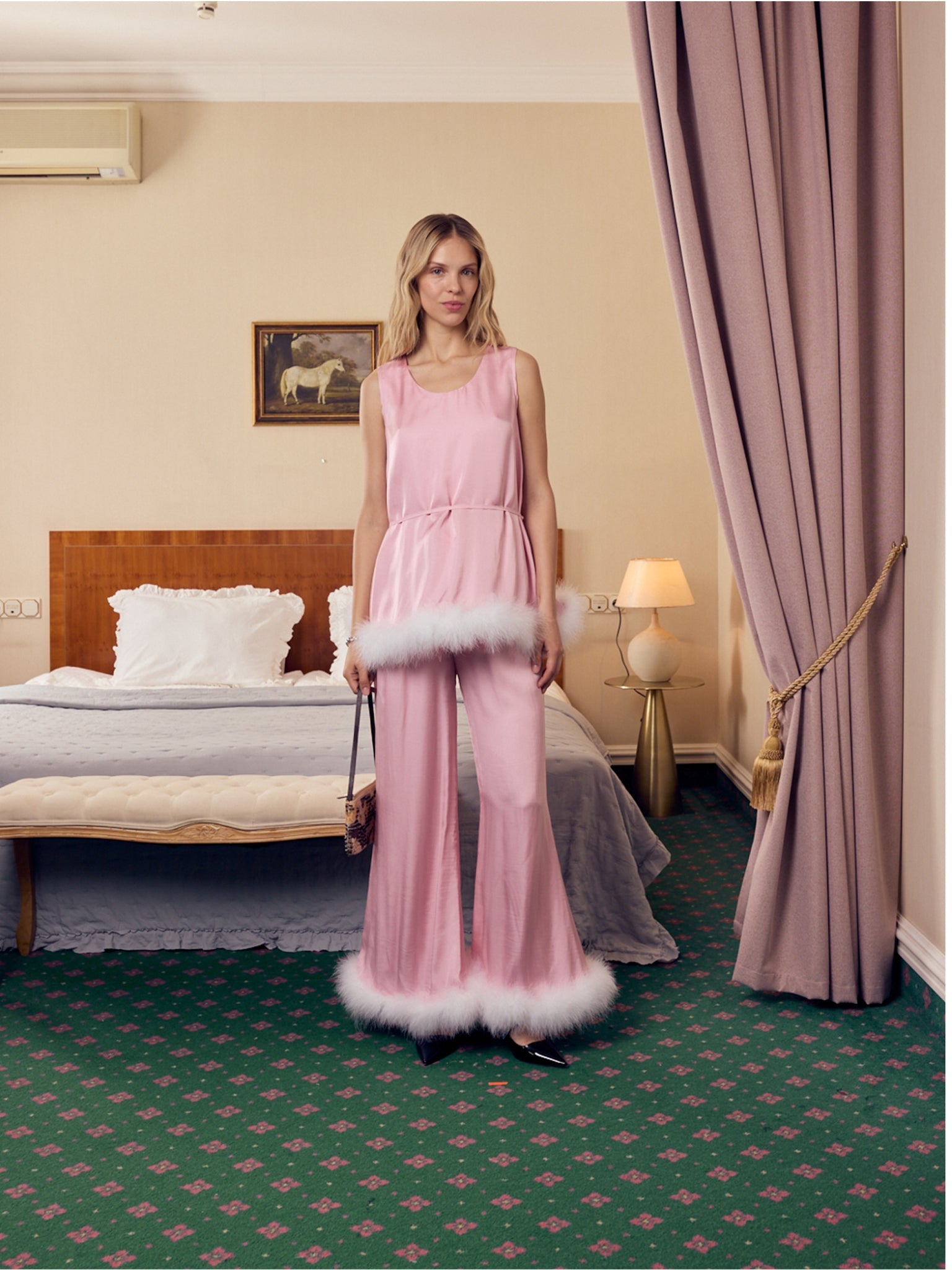 Woman wearing a pink sleeveless top and pants with white feather trim in a bedroom