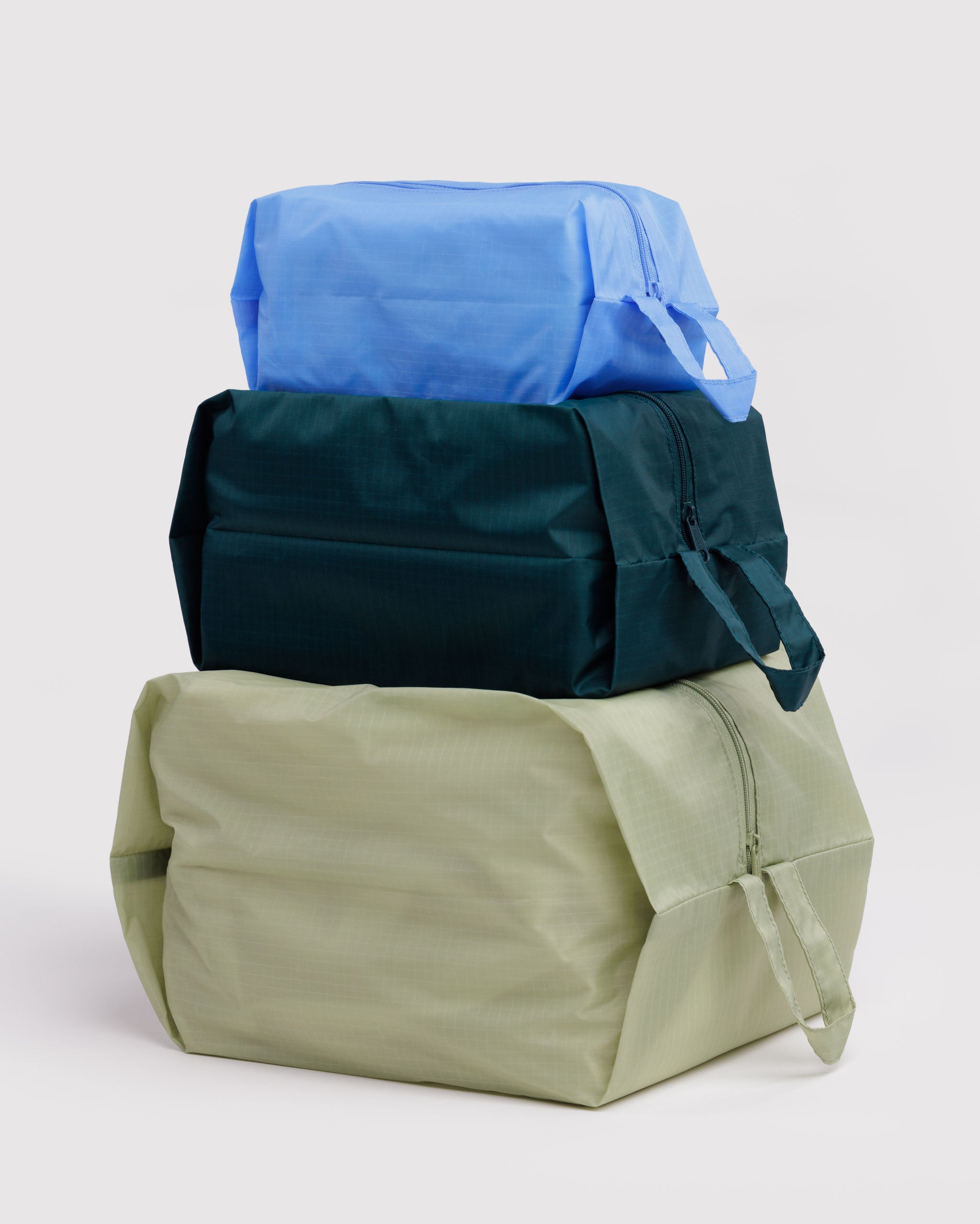 Three bags filled and stacked on top of each other with a blue, green, and teal colour scheme with zip closure and carry handle.