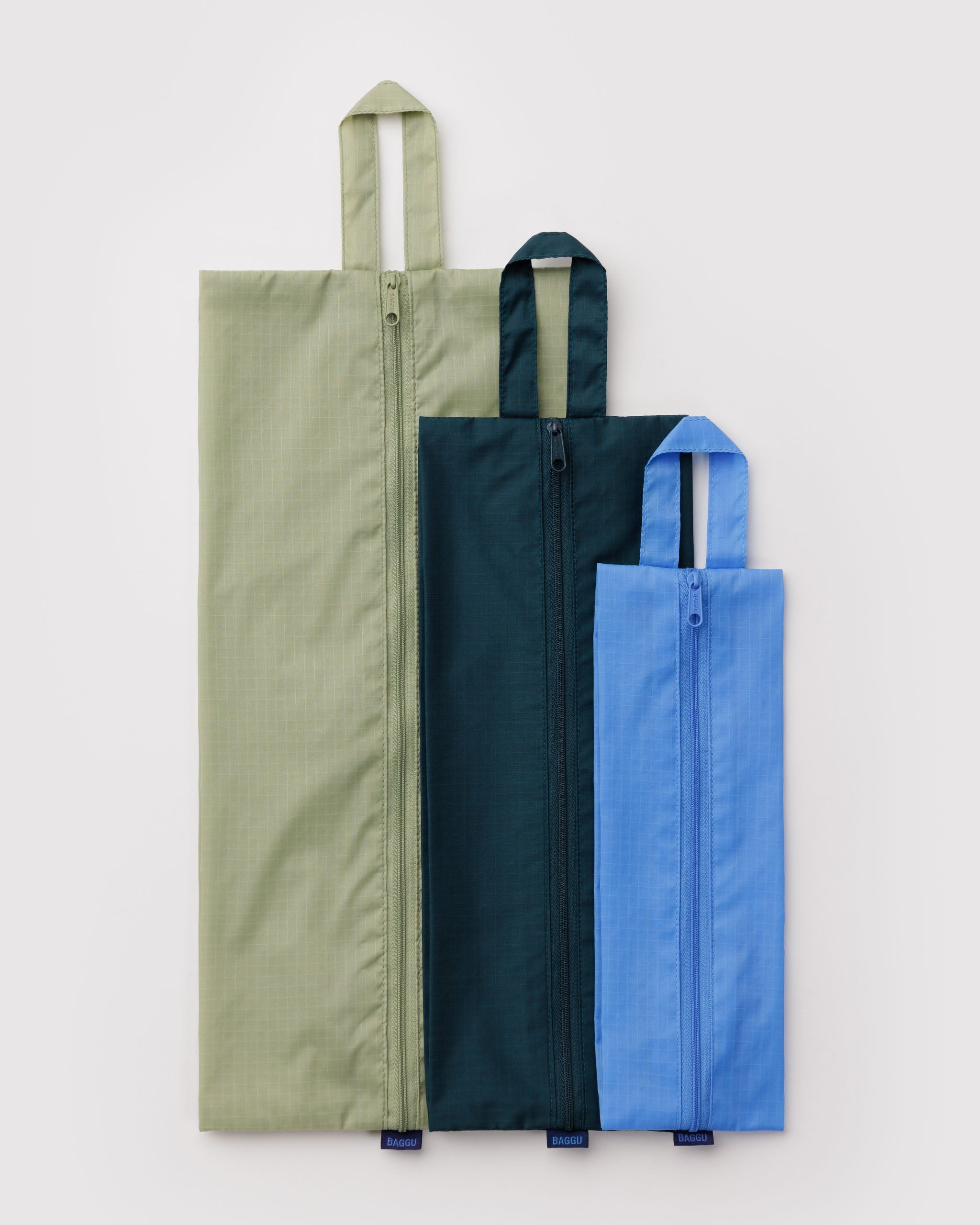 Three packing bags lying flat in green, teal, and blue with zips and hanging loop