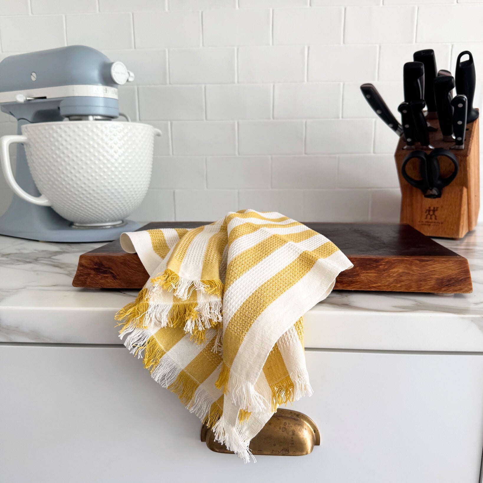 Yellow and white striped hand towel draped over a wooden cutting board on a kitchen counter with a mixer and knife block.