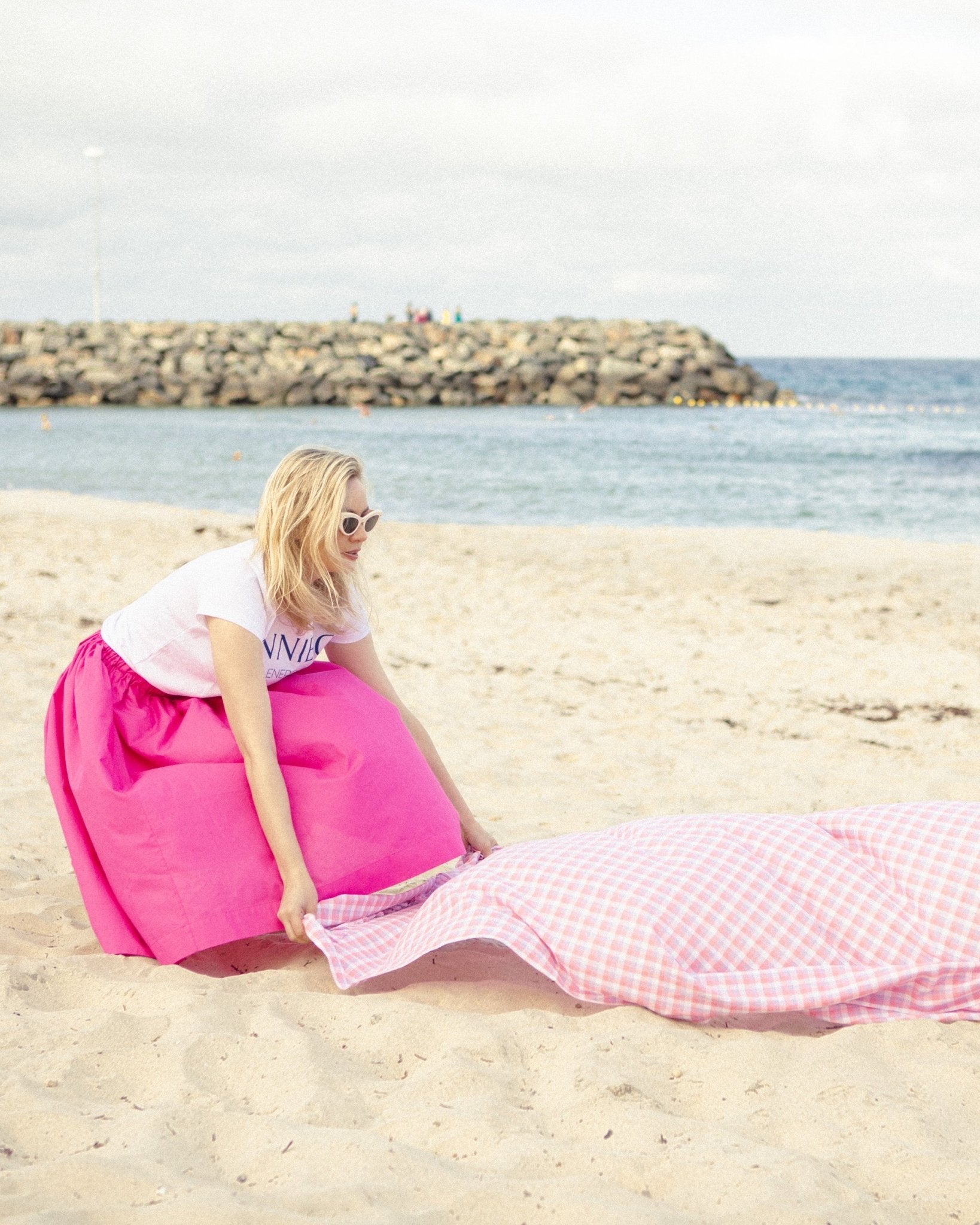 Woman placing the pink checked beach towel on sand at beach.