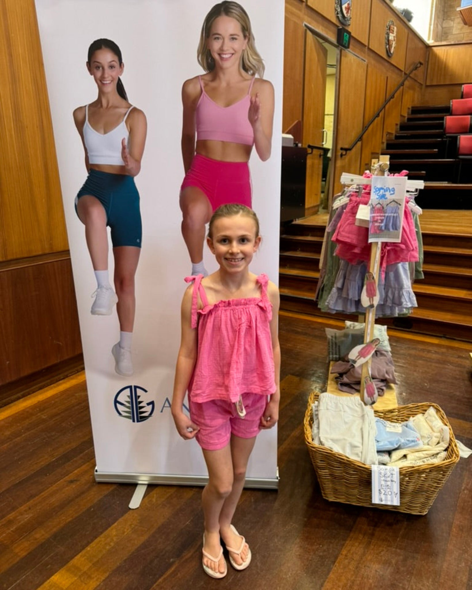 Girl in summer pink top and shorts set standing next to a banner display at a market.