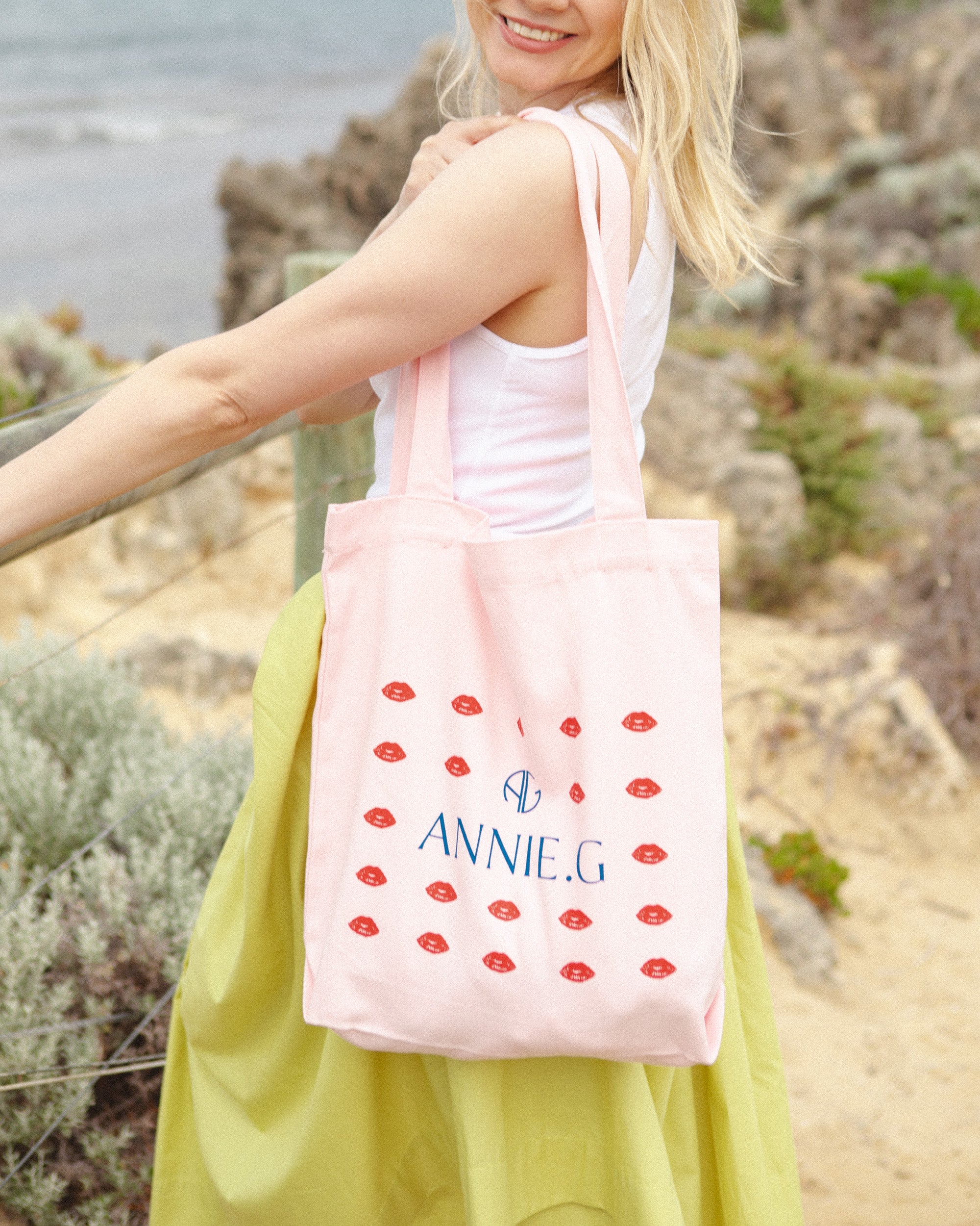 ANNIE_G-pink-with-small-red-lips-graphic-branded-cotton-canvas-tote-bag-on-girls-shoulder-at-the-beach