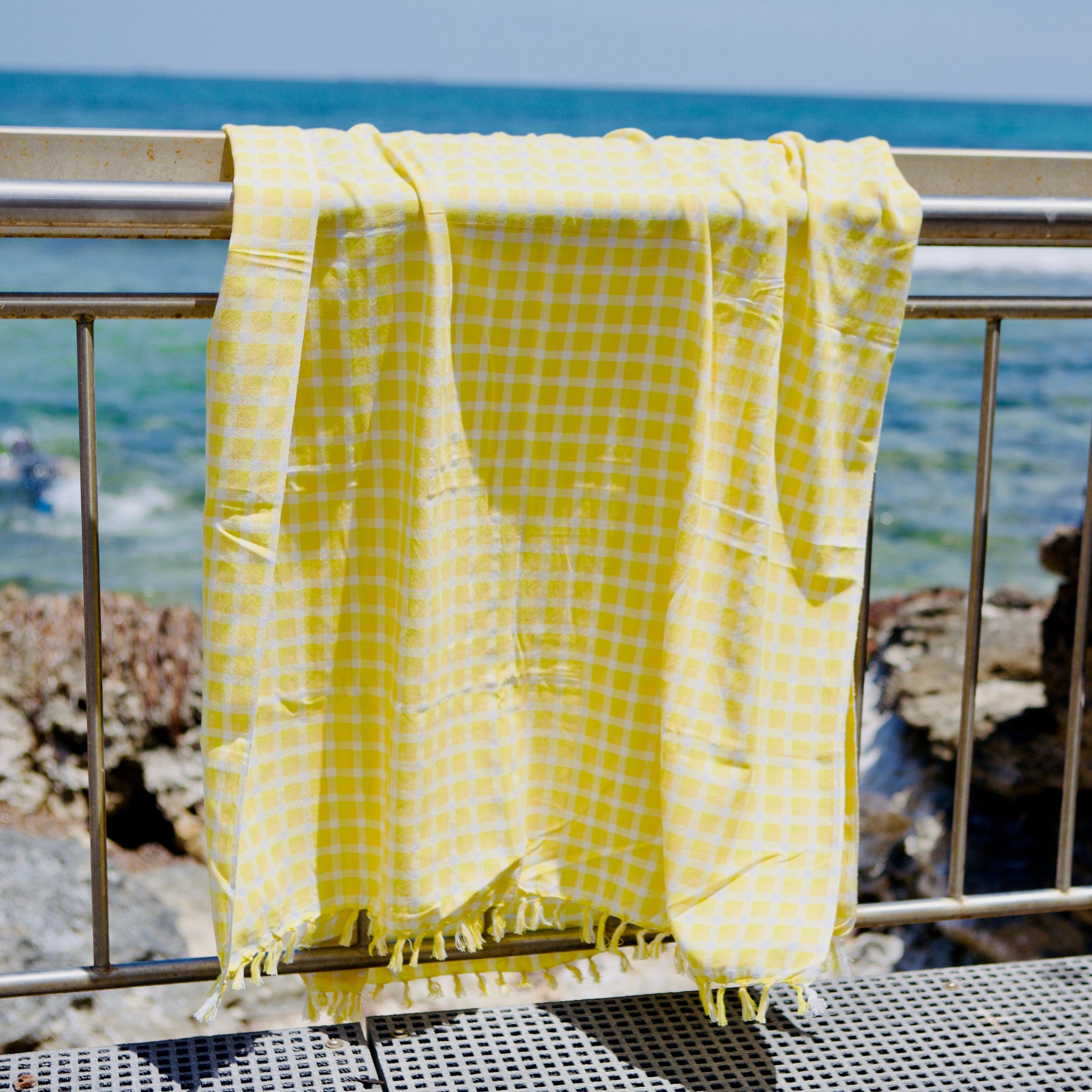 yellow-and-white-check-cotton-beach-towel-with-hand-knotted-tassels-hanging-over-rail-at-beach