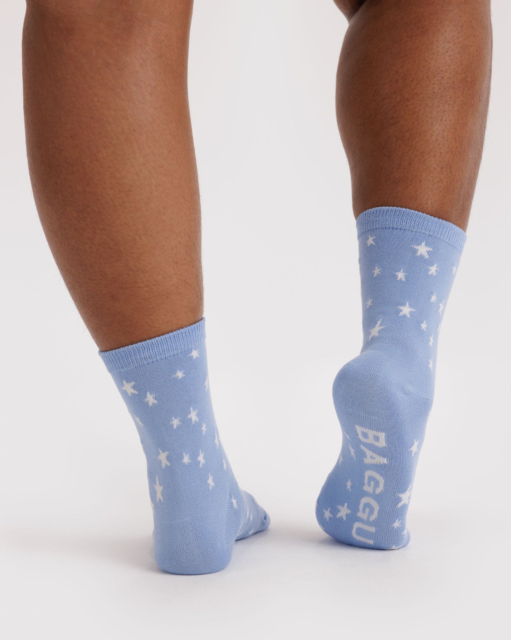 Blue socks with white star patterns and 'BAGGU' branding on sole worn by a person.