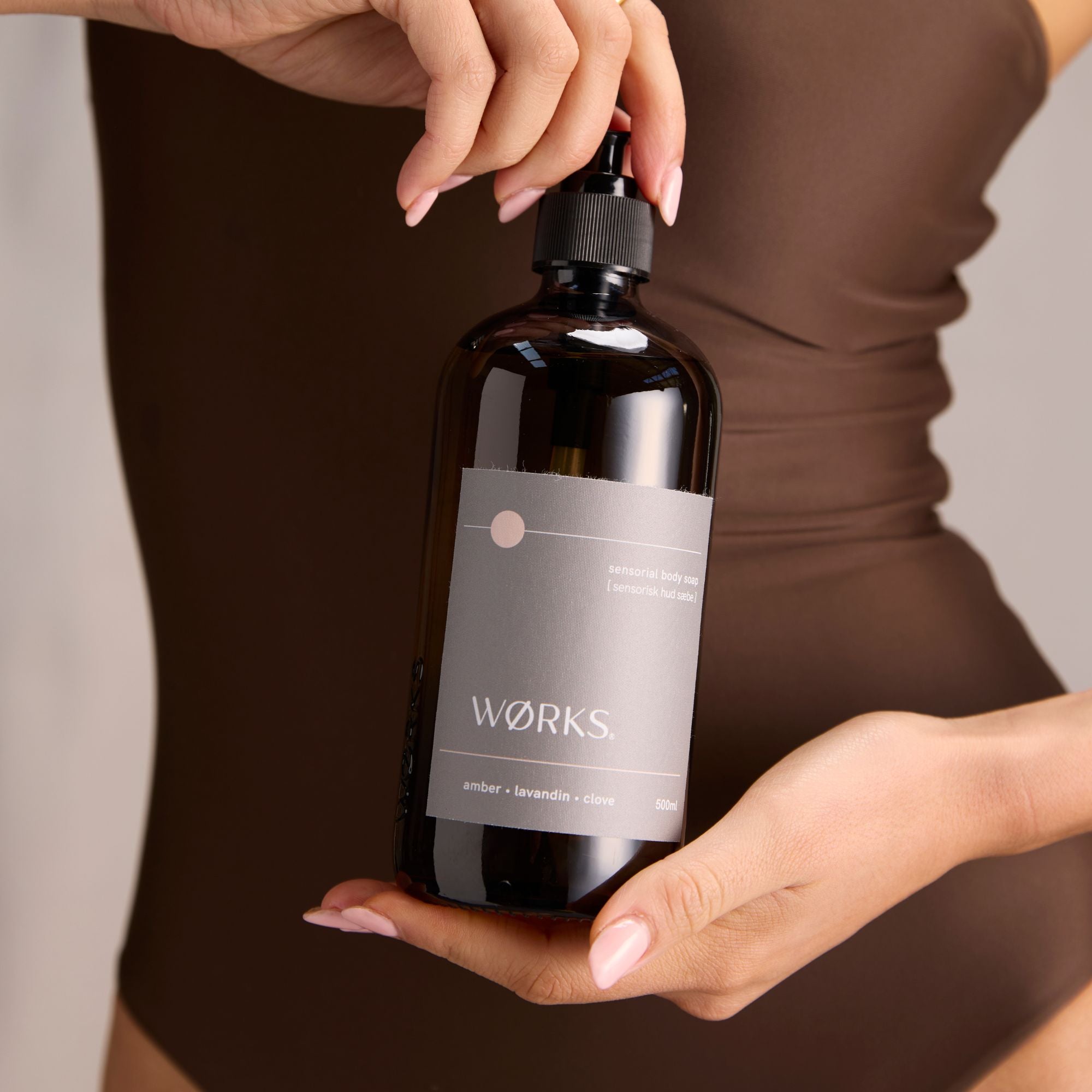 Person holding a pump bottle of body soap labelled 'Works' .