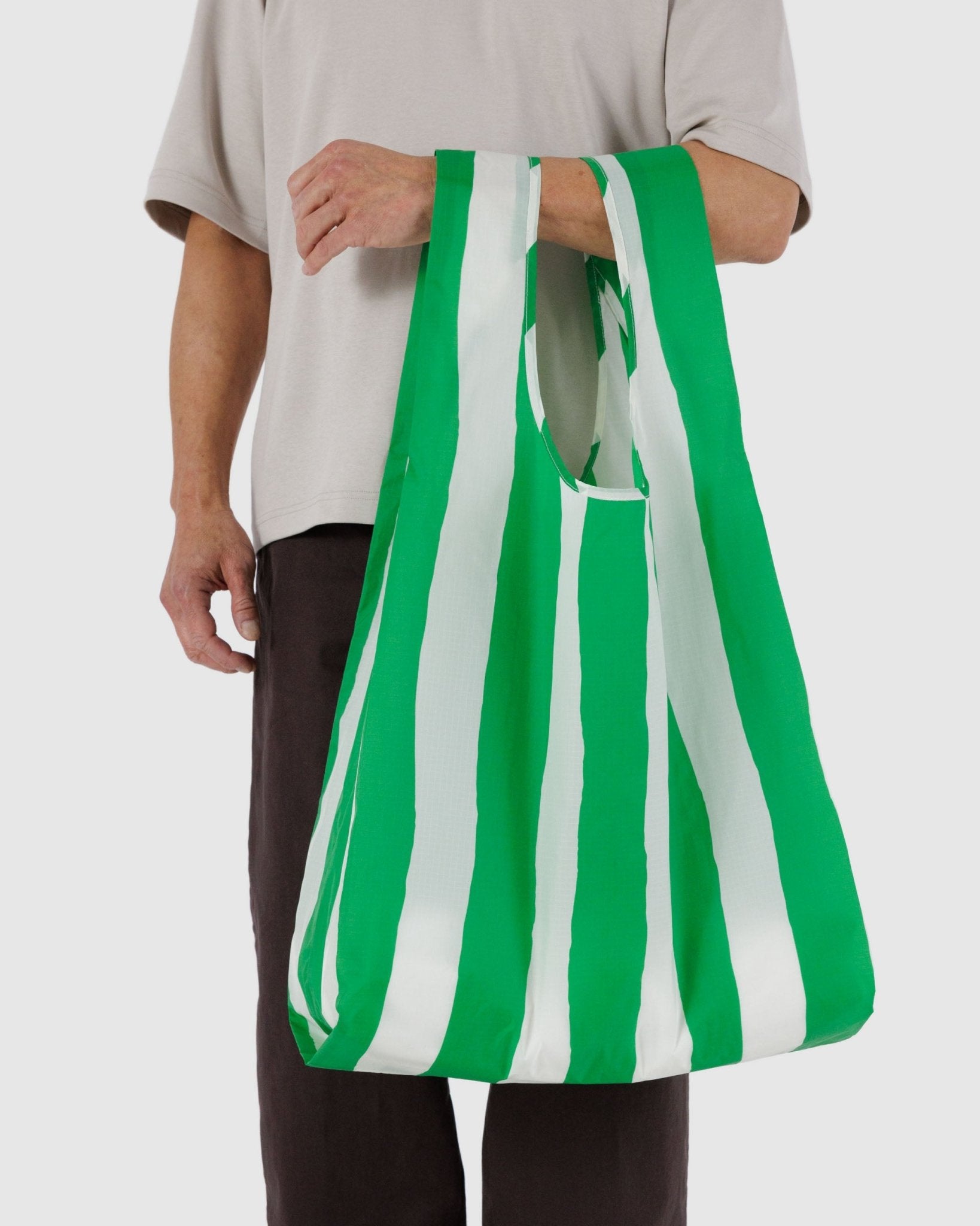 Man carrying a green and white wide stripe nylon reusable tote on arm.