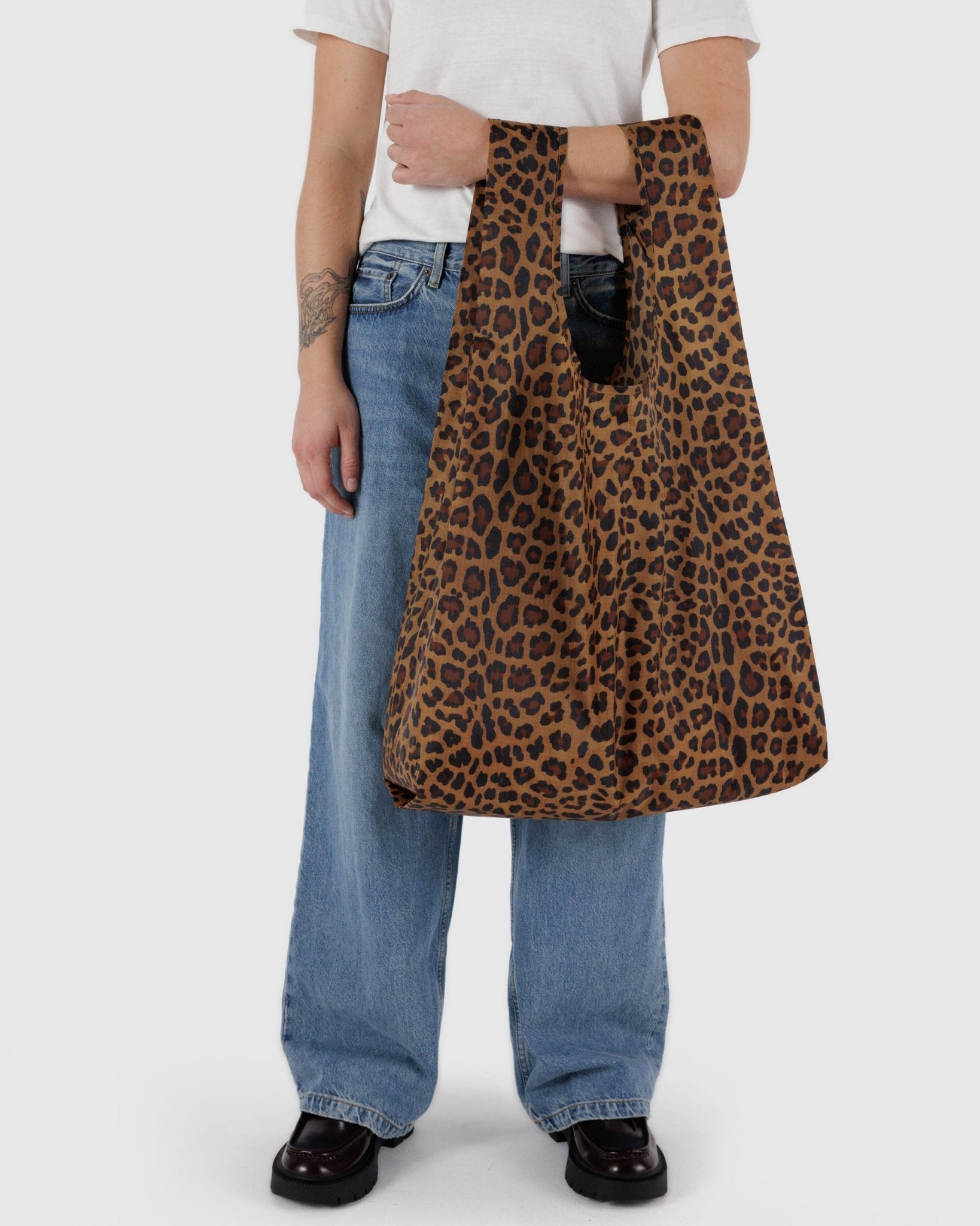 Person holding a leopard print tote bag on arm.