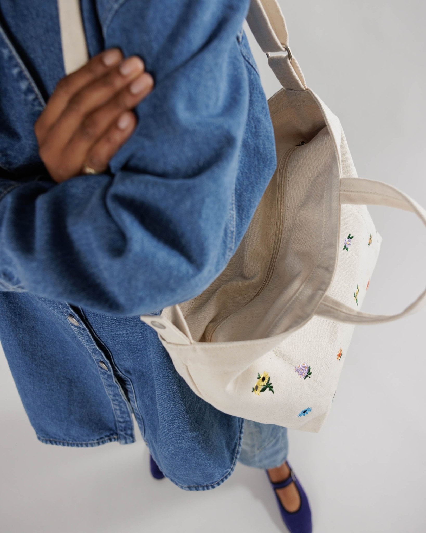 Person carrying a canvas tote with floral embroidery on shoulder.