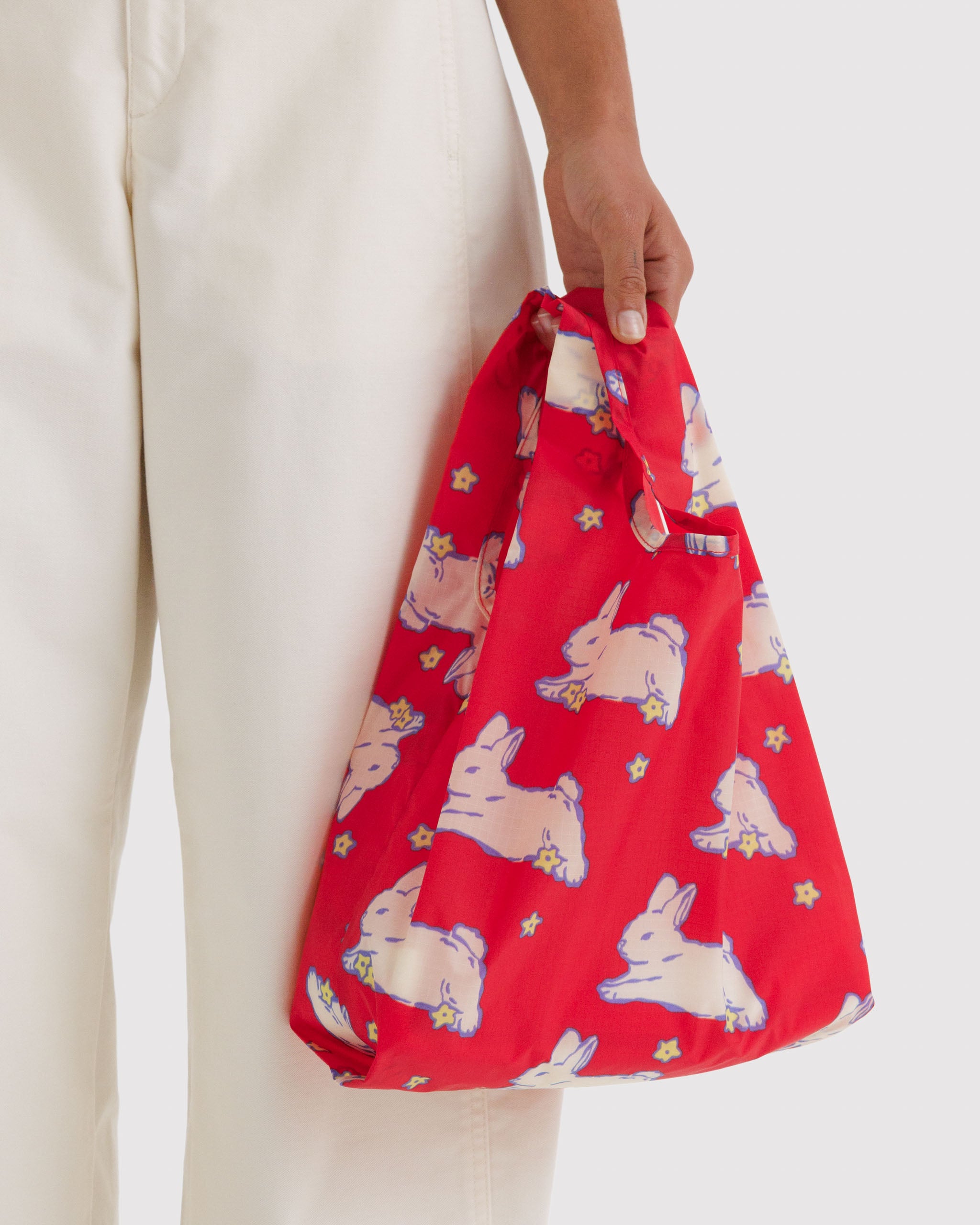 Red tote bag with white rabbit pattern held by a person's hand.