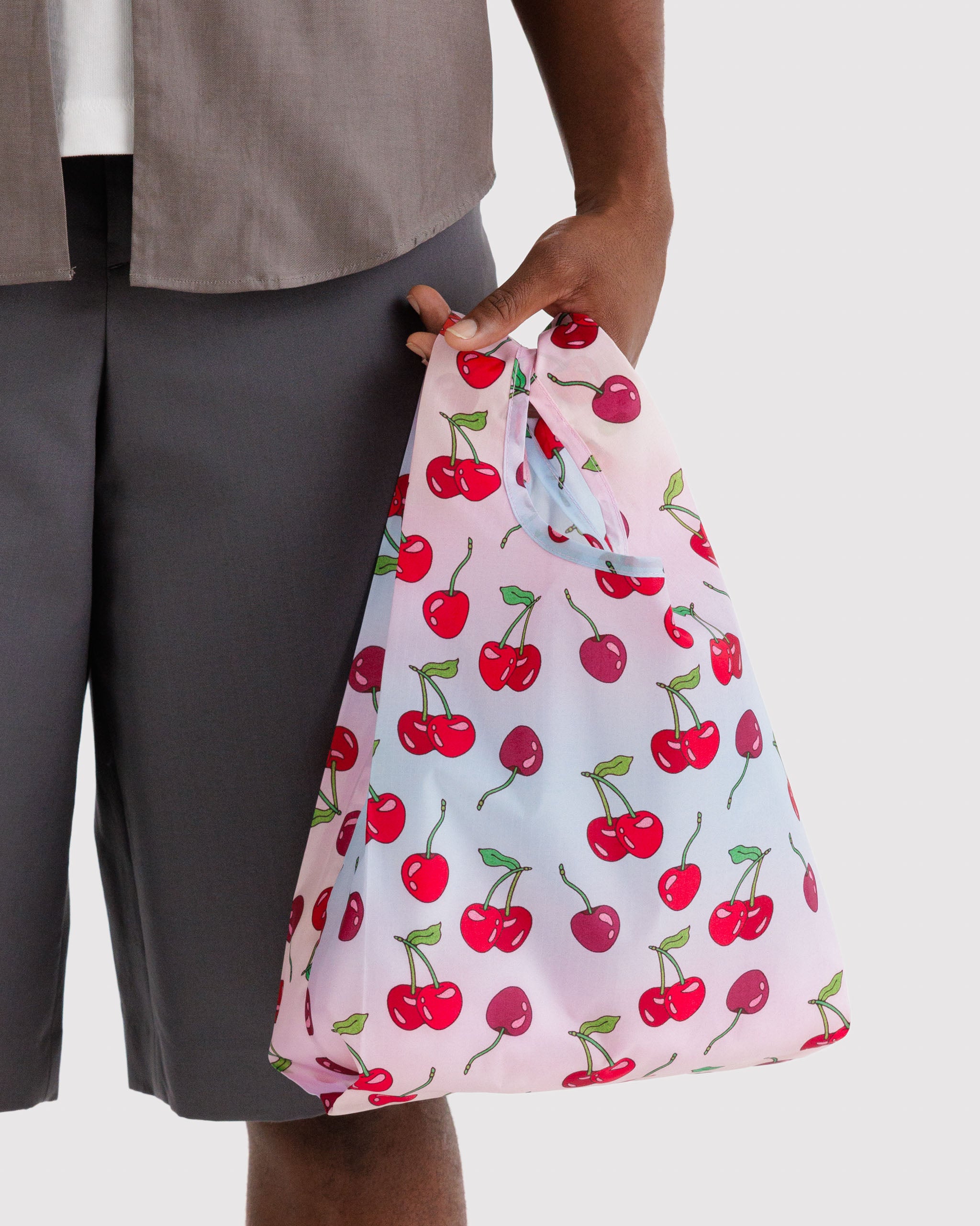 Person holding a reusable tote bag with cherry pattern.