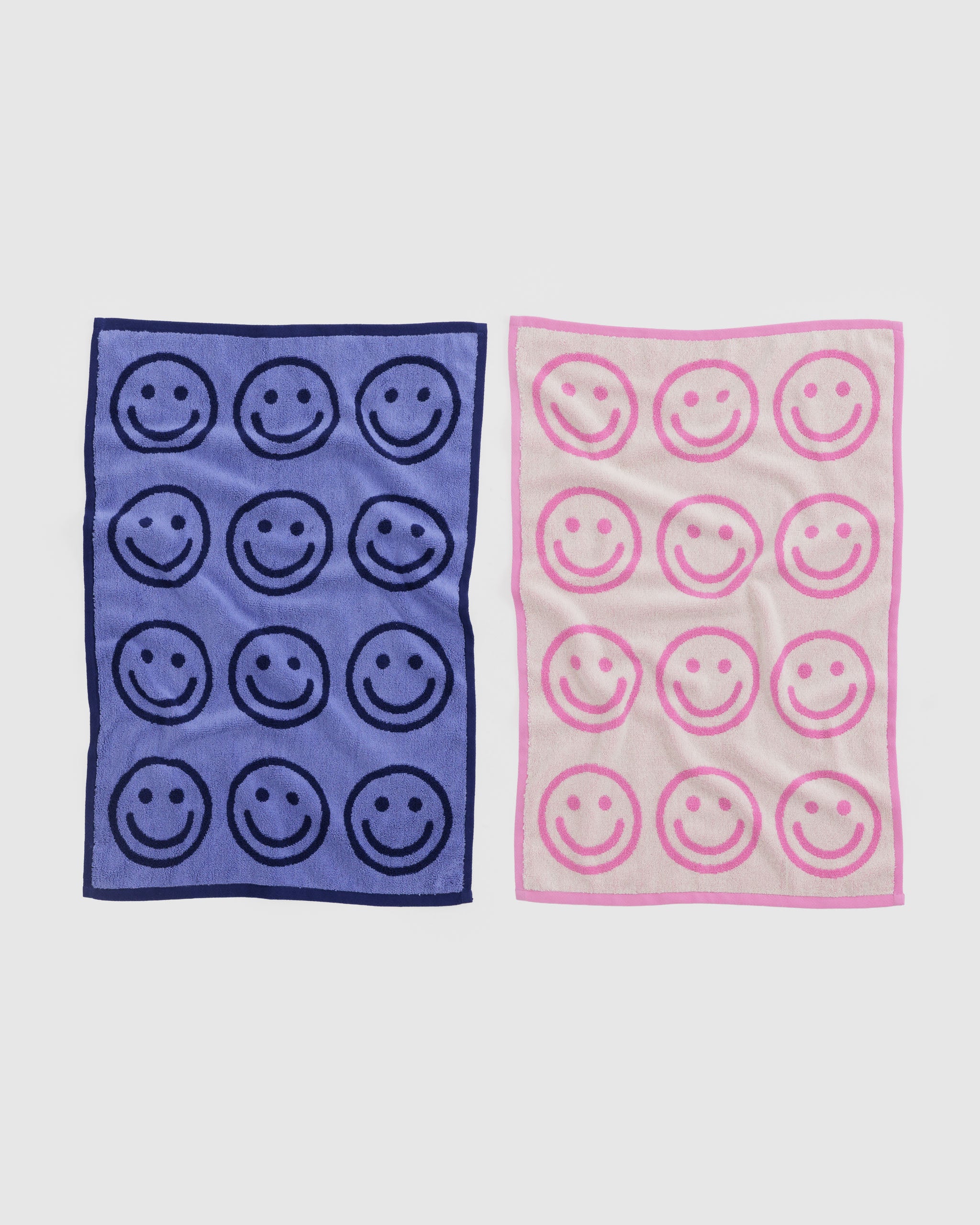 Two hand towels with smiley face patterns in a blue and a pink.