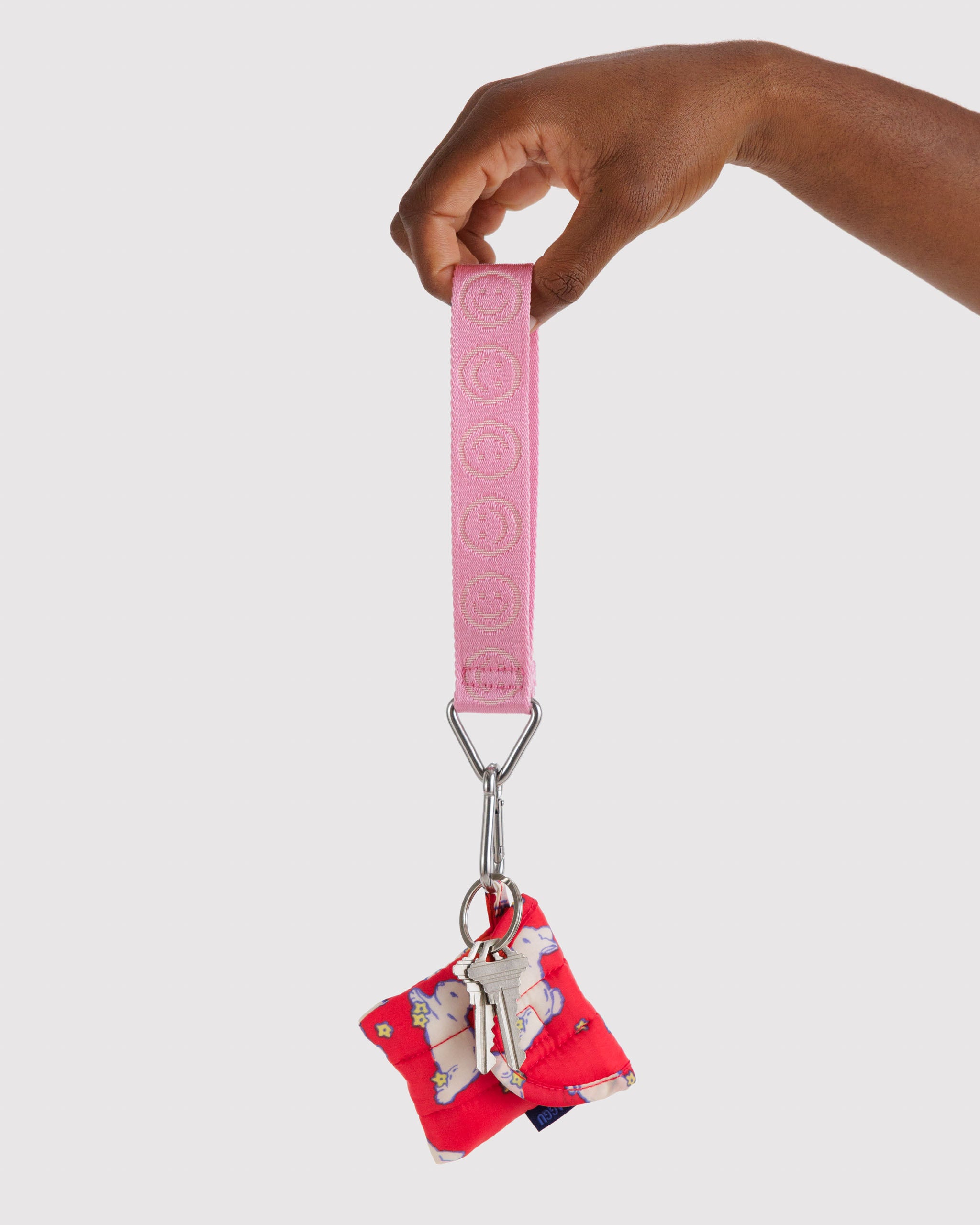 Pink keychain with smiley face print on webbing strap with metal triangular ring and clip attached to a red earbuds case and keys - ANNIEG