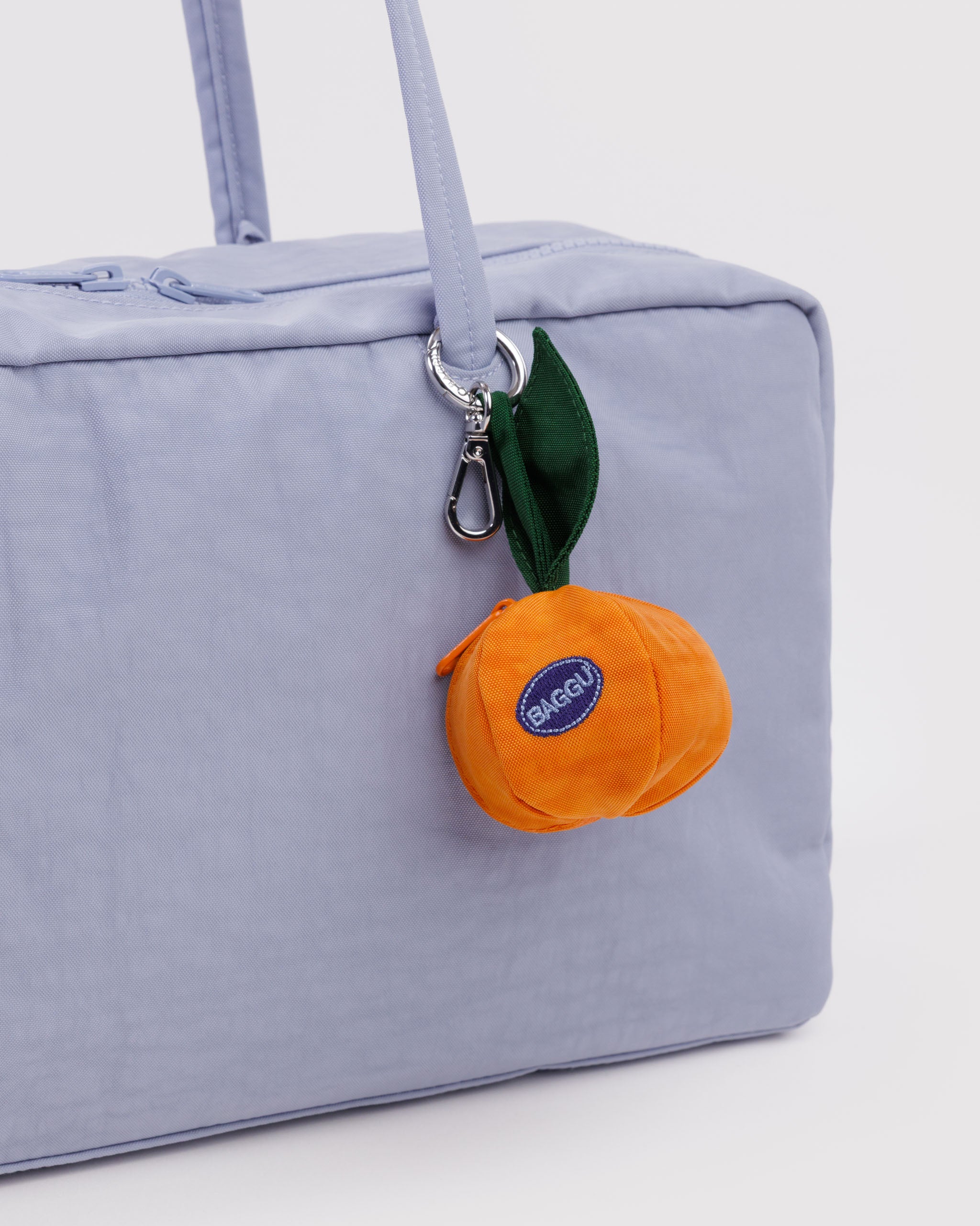 Light blue coloured bag with an orange-shaped bag charm with keychain attached to handle strap.