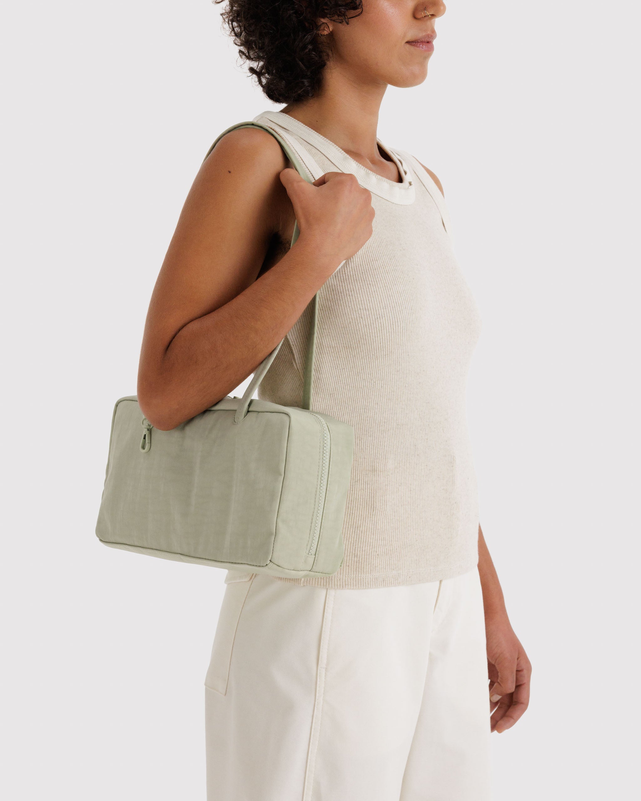 Woman holding the double long handles of a light green handbag on shoulders.