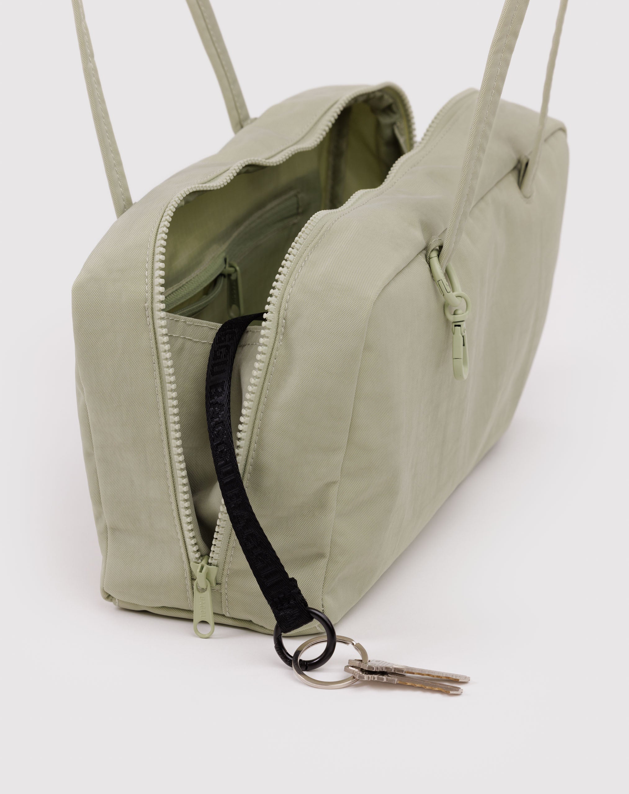 Light green bag with top zips open and a black keychain holding keys.