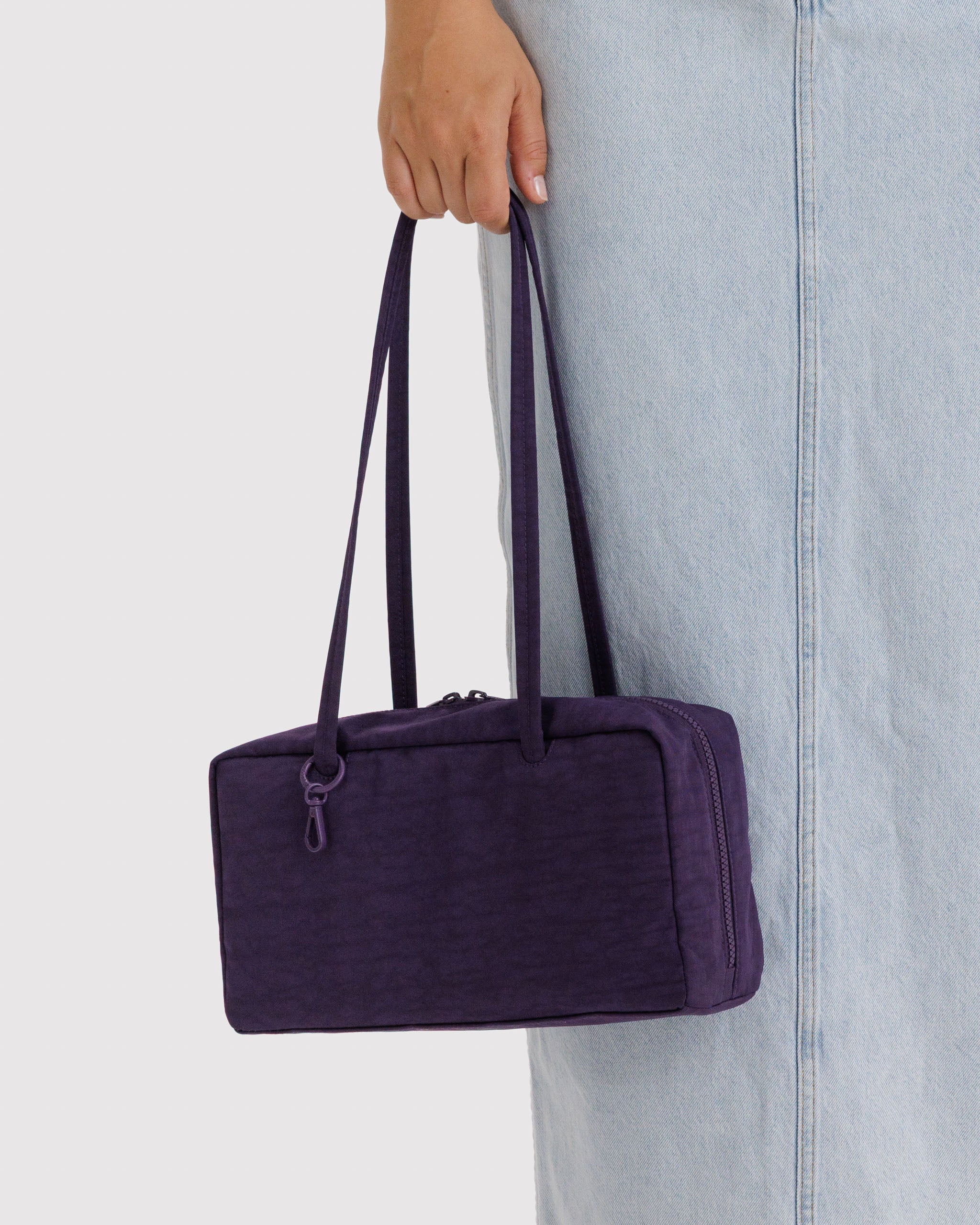 Person holding double long handles of a purple handbag.
