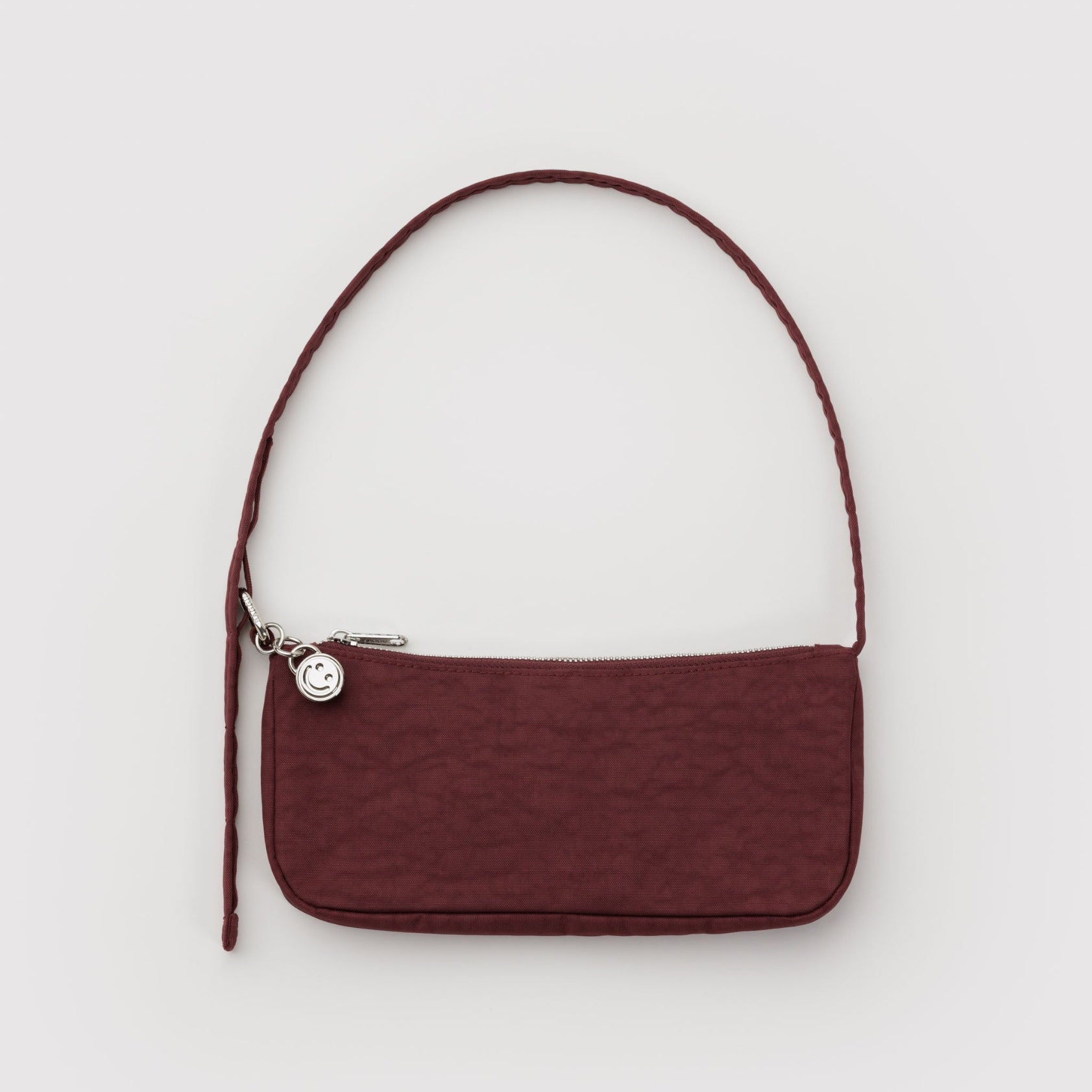 Small mahogany print handbag with adjustable shoulder strap with metal hardware, clasp, zip and smiley face charm.