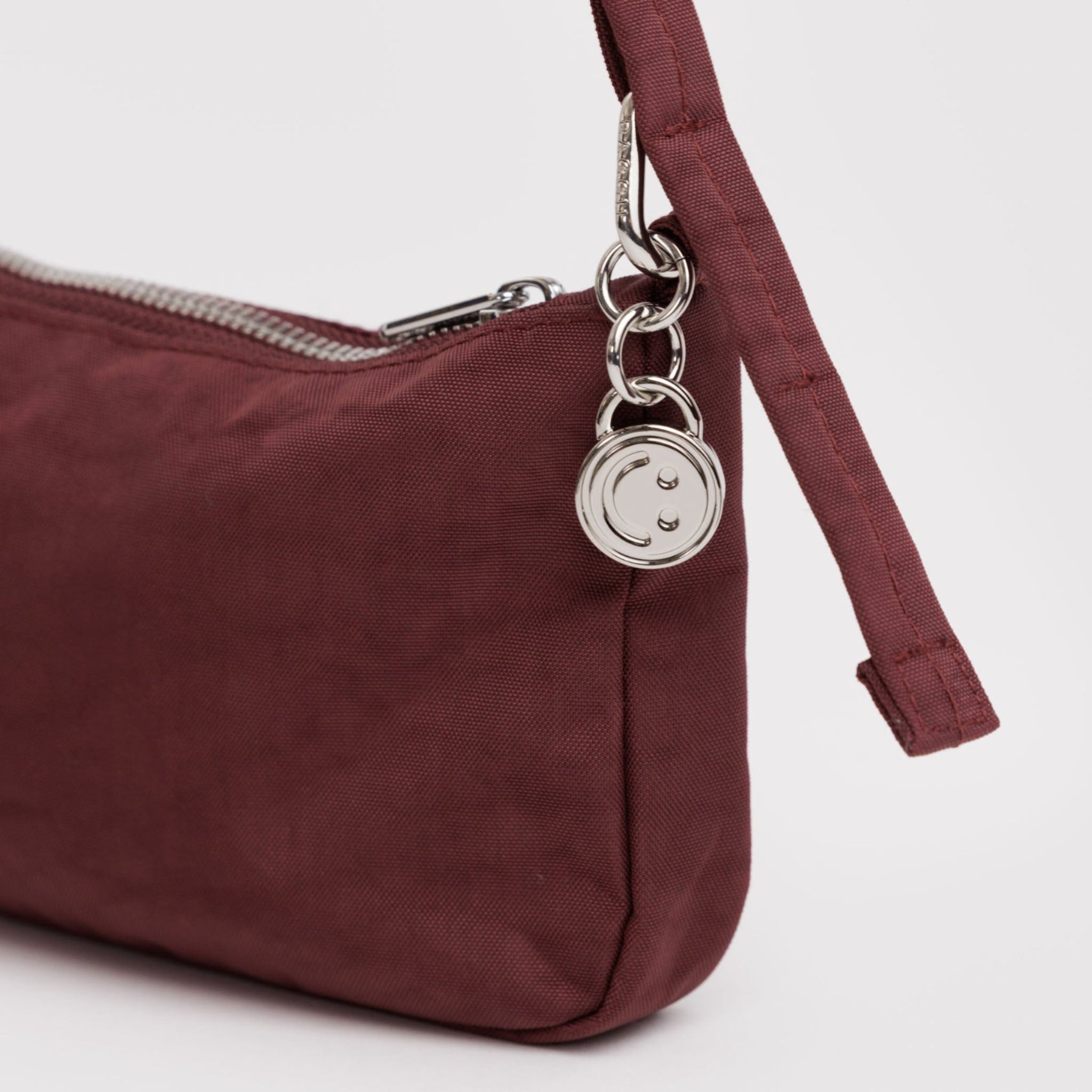Small nylon mahogany handbag with an adjustable strap and silver hardware clasp, smiley face charm and zip.