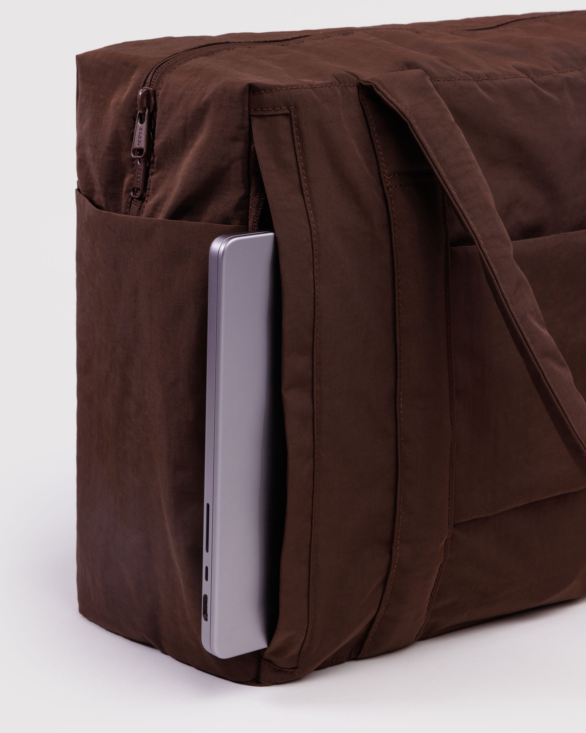 Brown duffle bag with a laptop inside an outside pocket with zip top, luggage sleeve and carry handles.