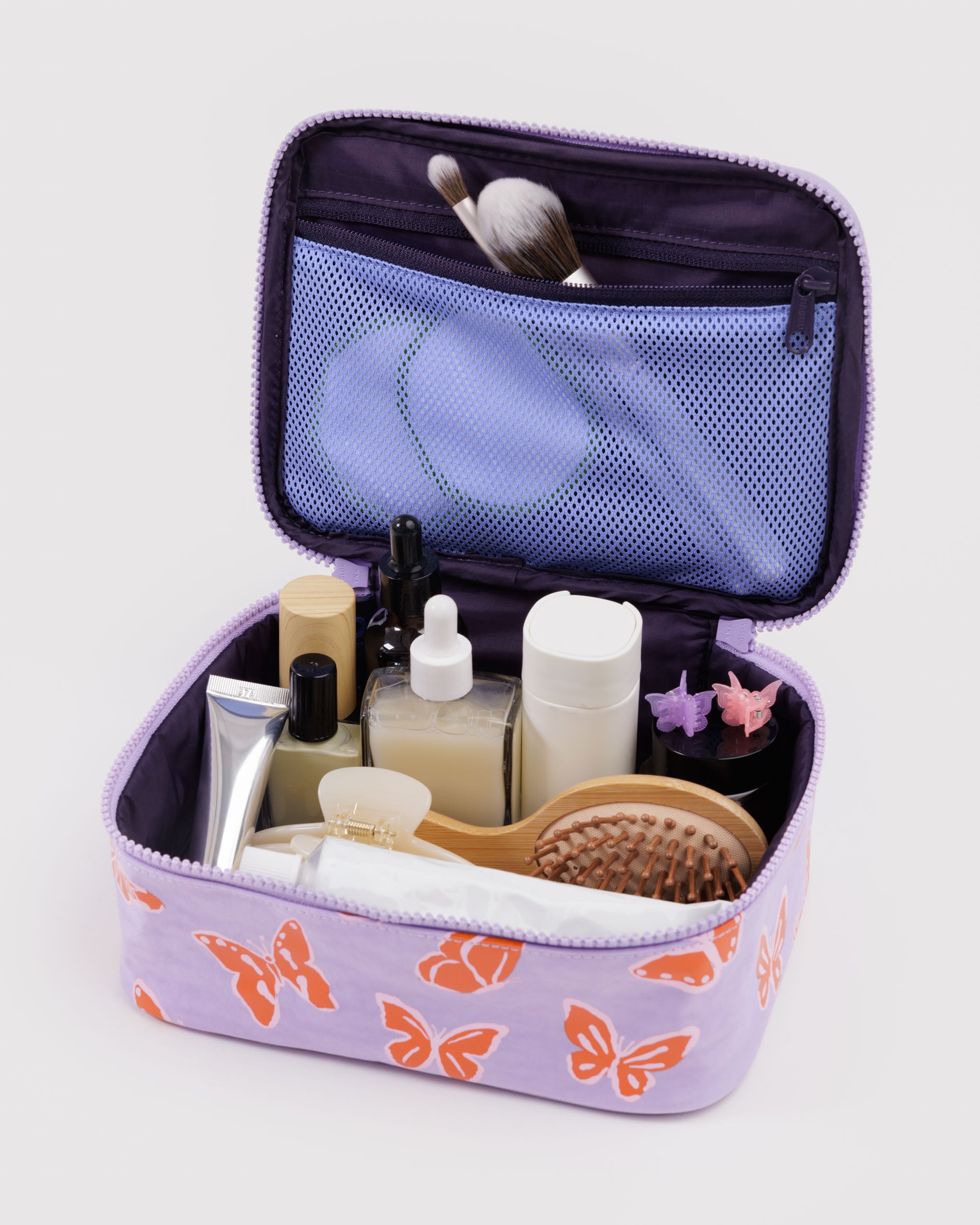 Purple cosmetic bag with butterfly pattern containing various toiletries with brushes in the mesh zip pouch on the inside of the lid.