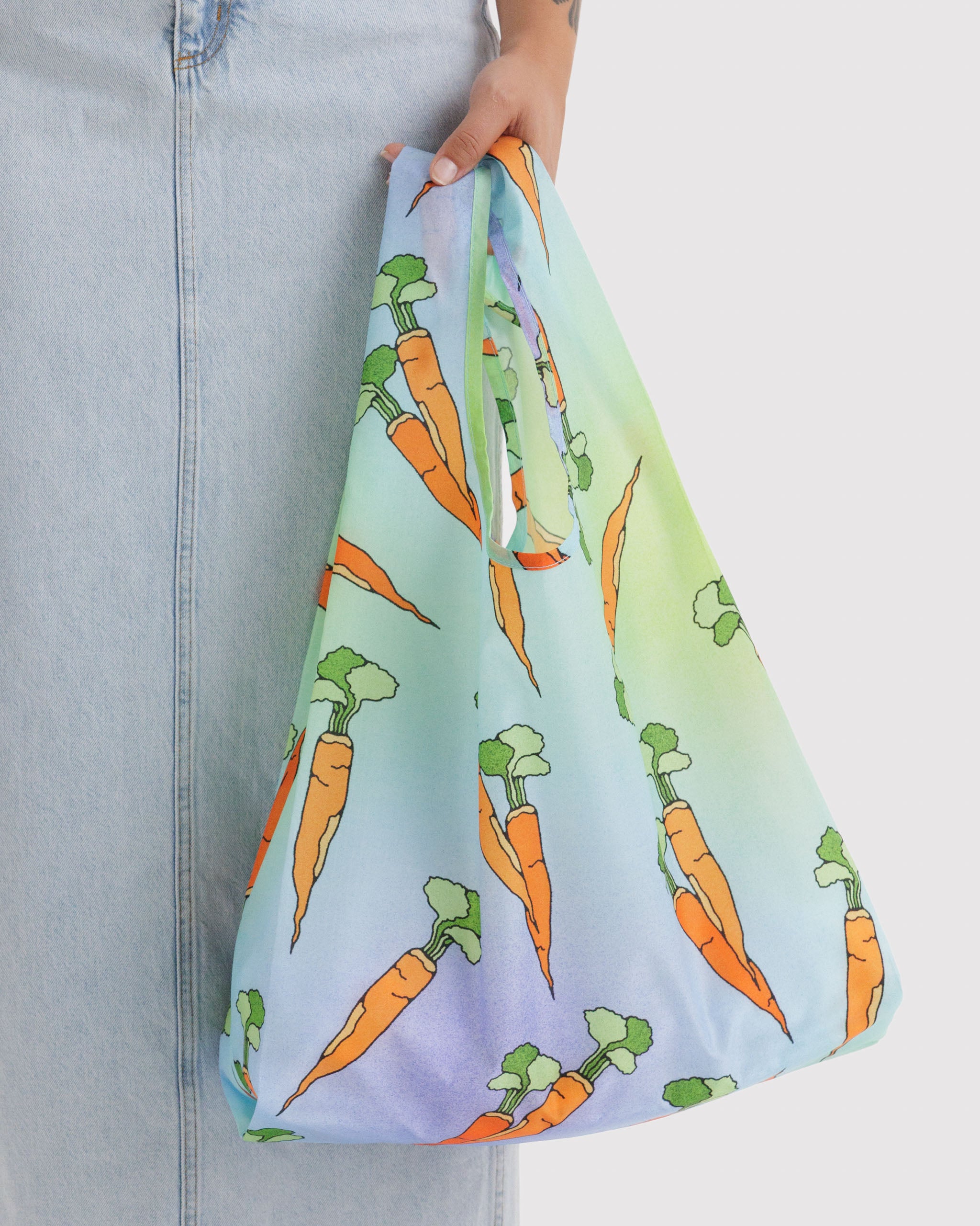 Reusable tote bag with carrot pattern on blue and green background held in a person's hand.