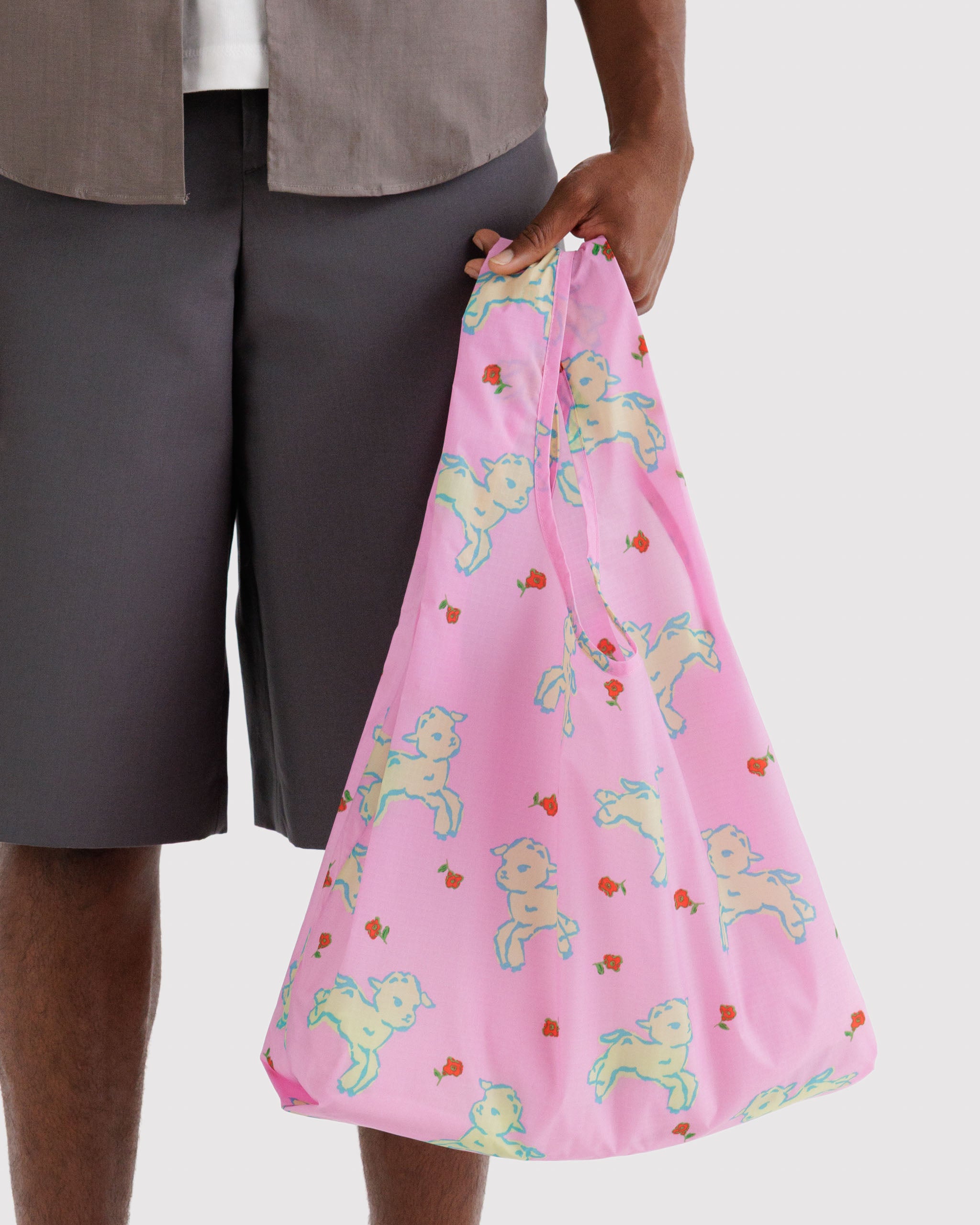 Person holding a pink reusable tote bag with white lambs and red flowers designs.