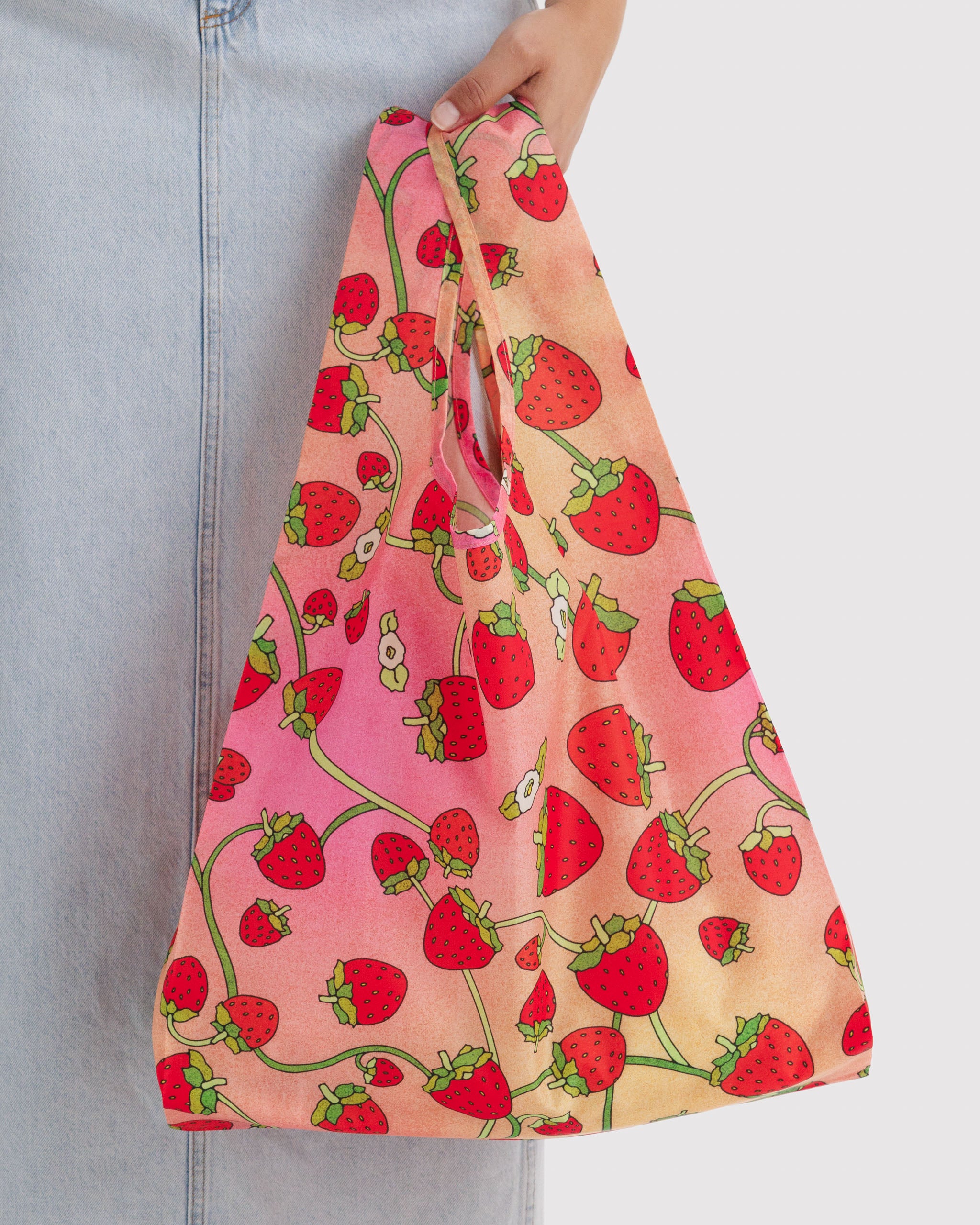 Reusable bag with strawberry and whhite flowers pattern held by a person in the hand.
