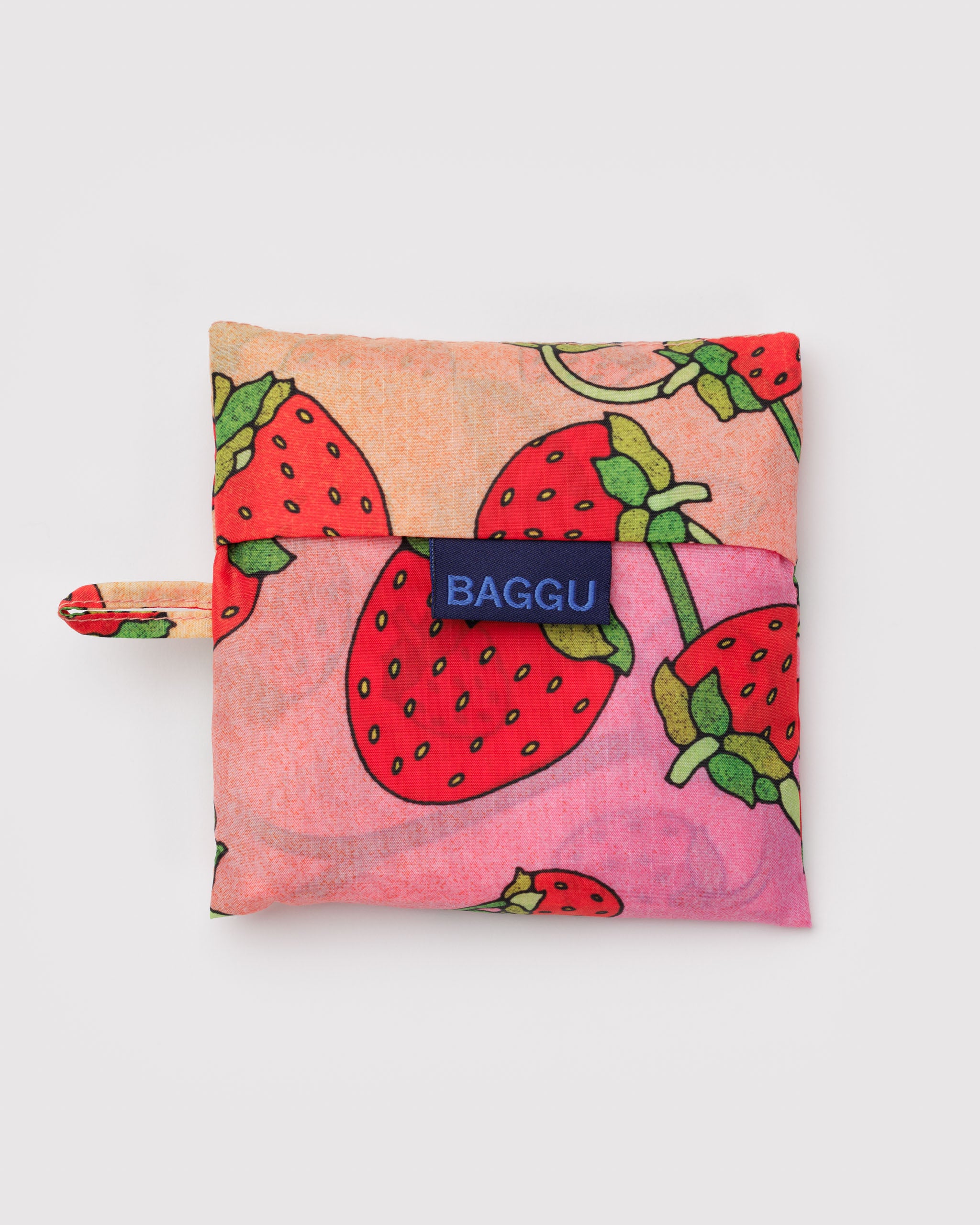 Pink and orange reusable bag with strawberry pattern and 'Baggu' brand logo with hanging loop.