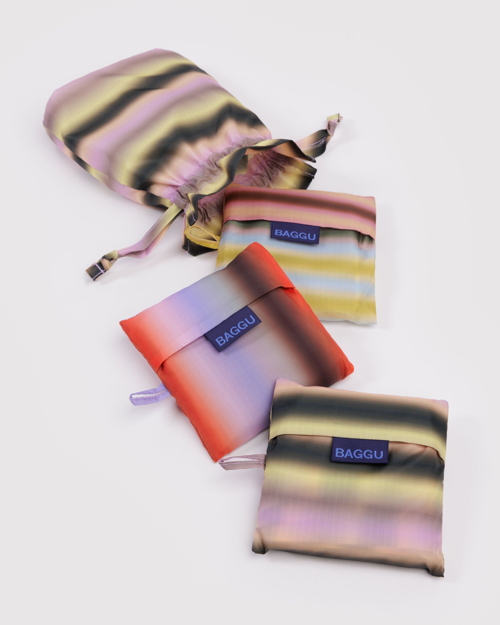 Set of 3 colourful bags with hanging loops and 'BAGGU' branding and a multistripe drawstring pouch they fit inside of.