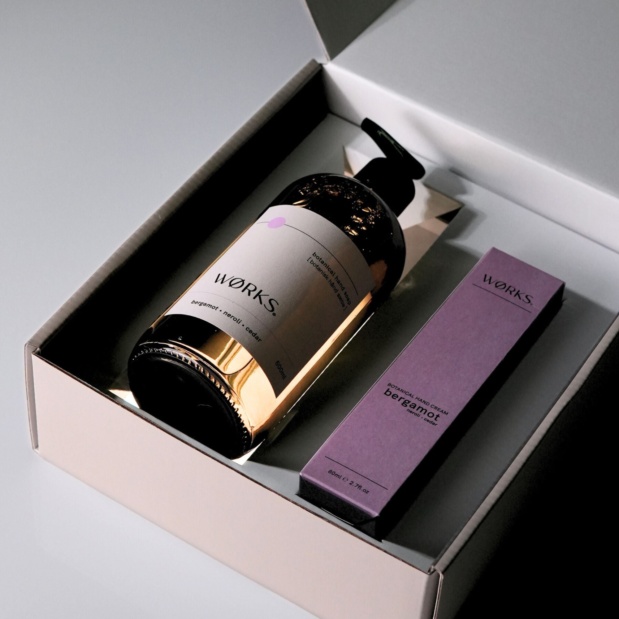 A brown, glass pump bottle and a purple box of 'WORKS' products in a grey gift box with lid open.