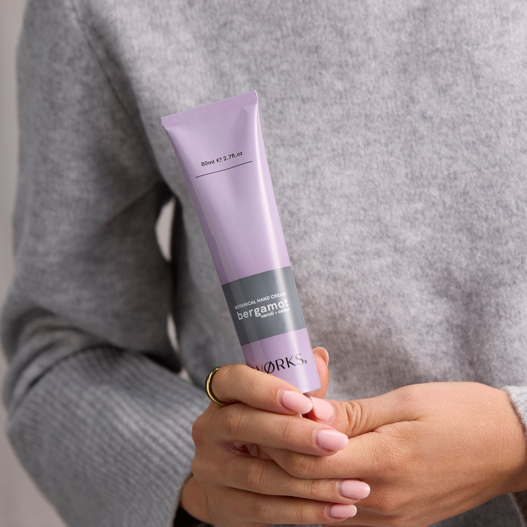 Person holding a purple tube of skincare product with 'works' branding.
