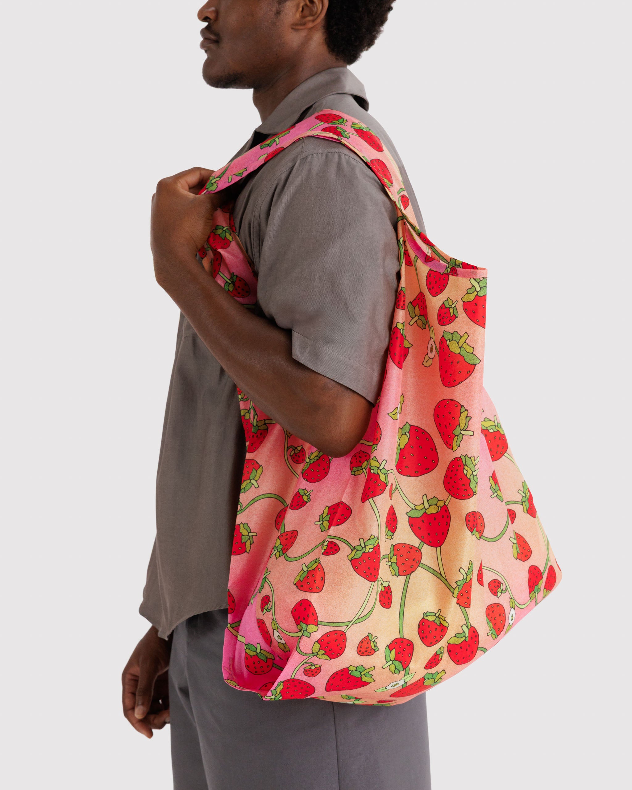 Man holding a strawberry and white blossom patterned reusable bag on shoulder.