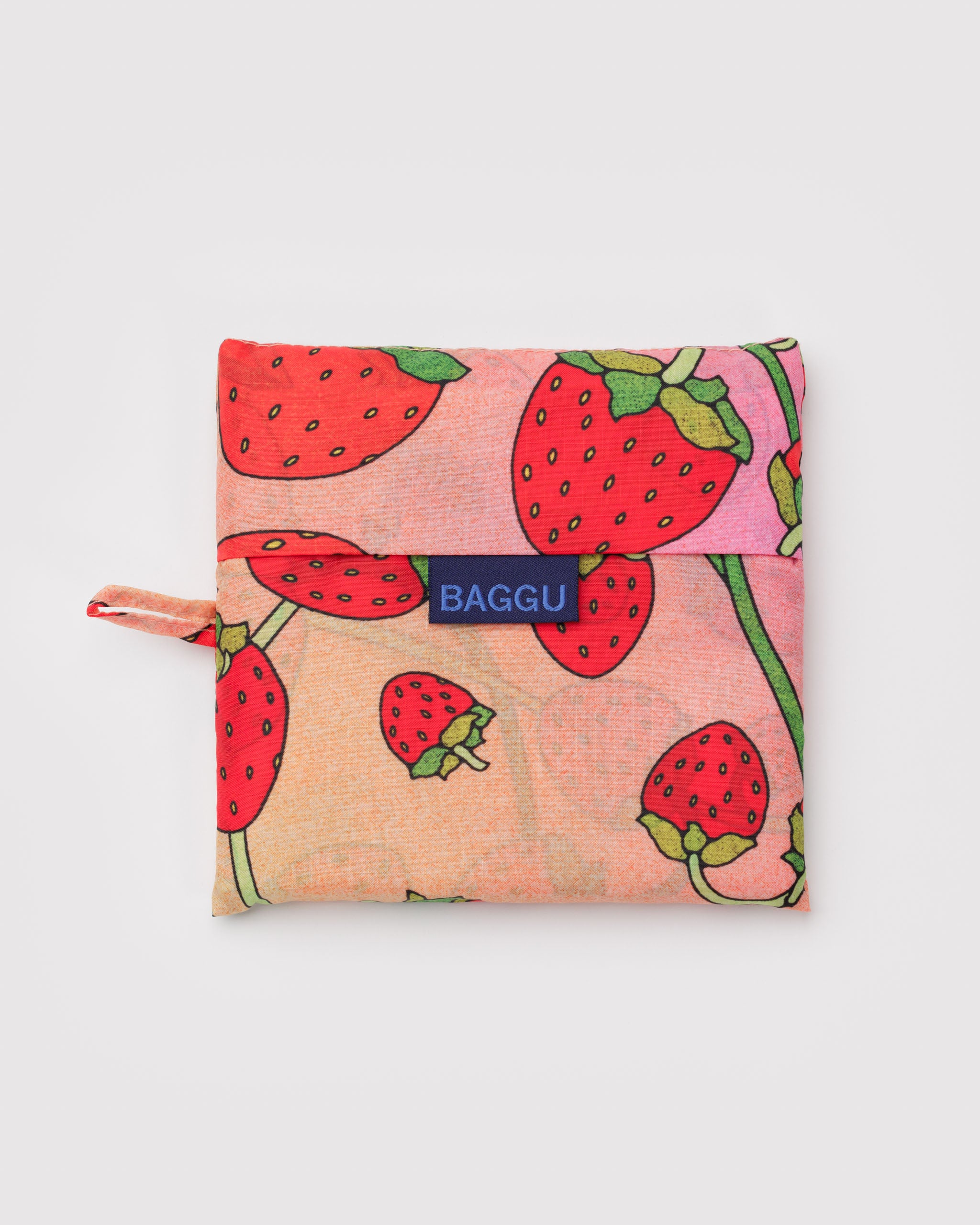 Pink reusable bag with strawberry and white blossom pattern and a blue 'BAGGU' logo.