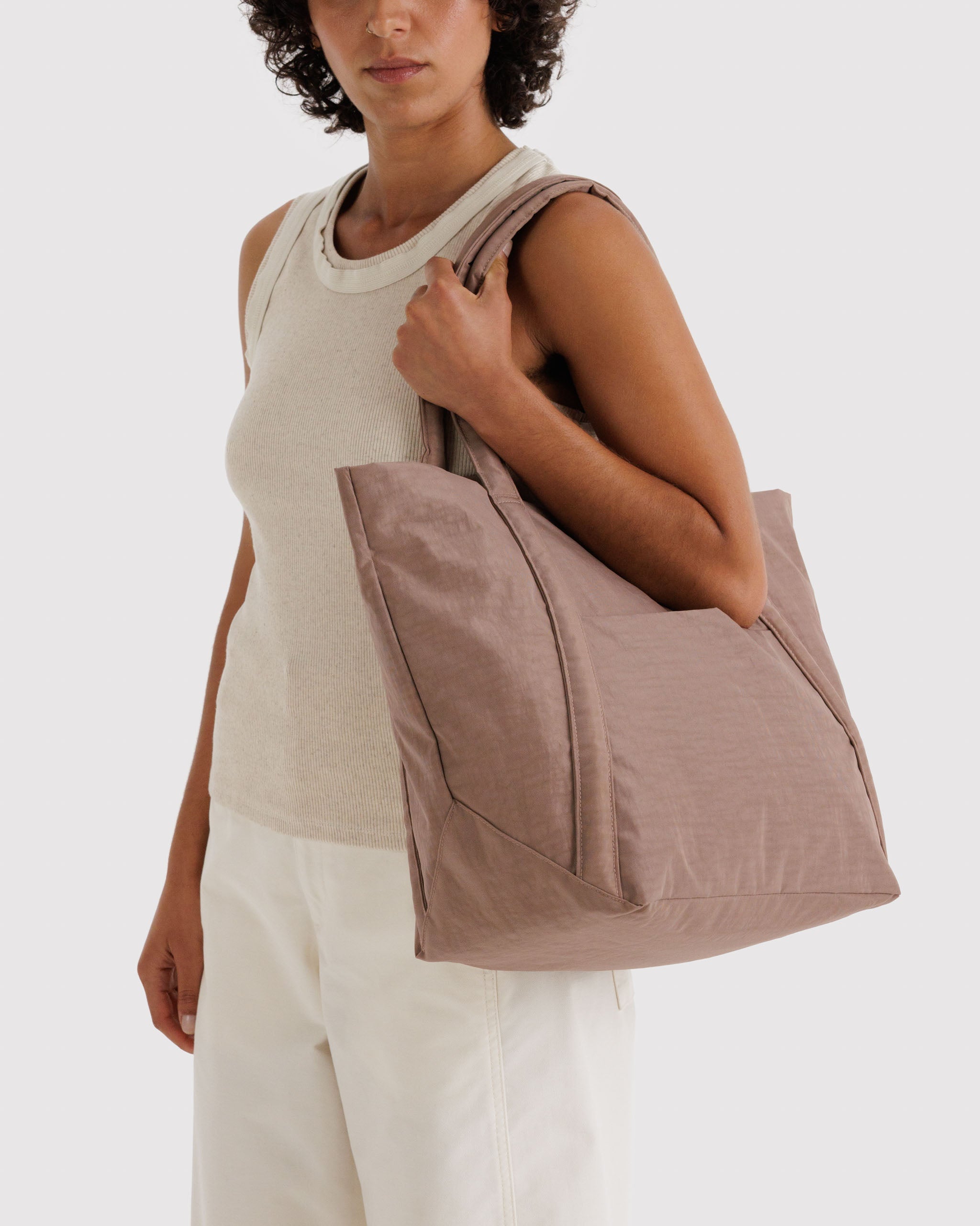 Woman holding a brown tote bag on shoulder.