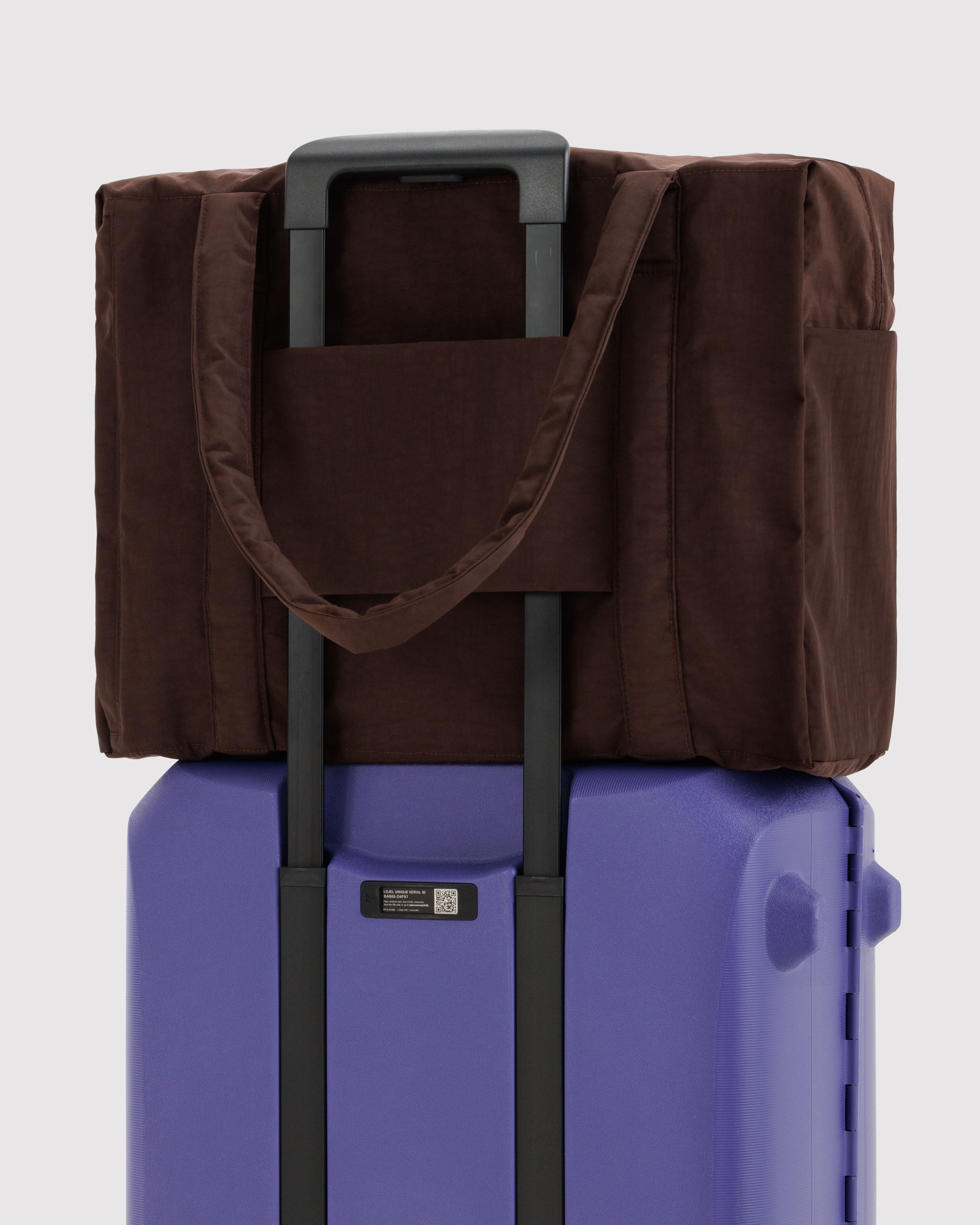 Brown tote bag with trolley sleeve on handles of a purple suitcase.