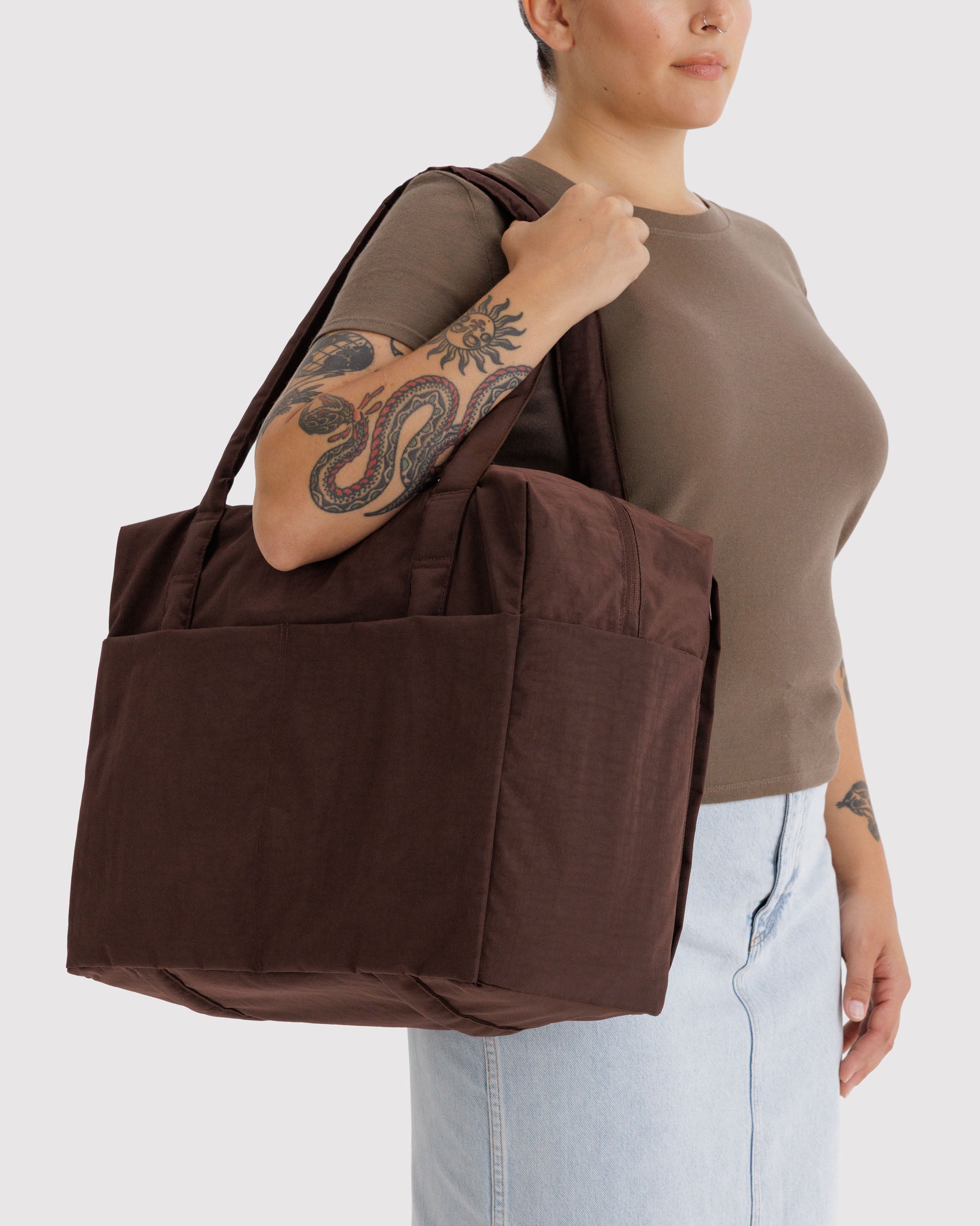 Woman holding a brown tote bag on shoulder.