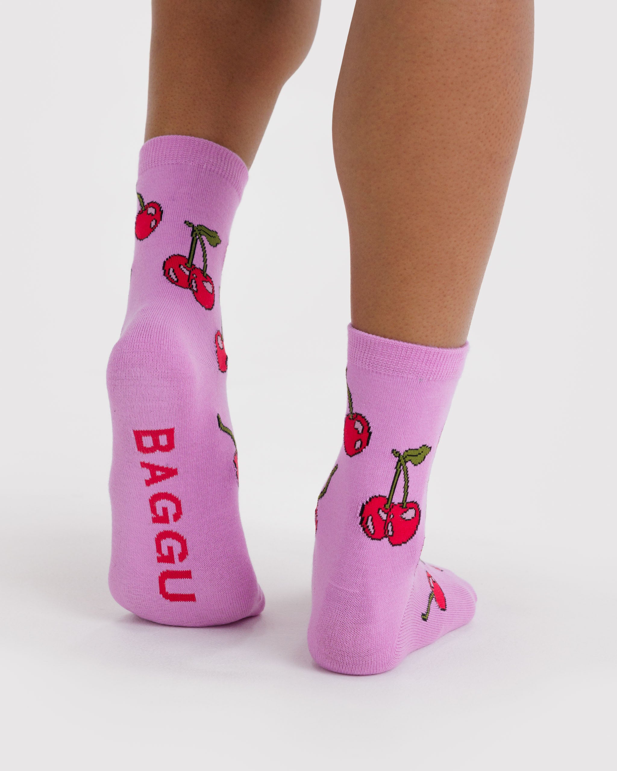 Person wearing pink socks with cherry design and 'BAGGU' branding on sole.