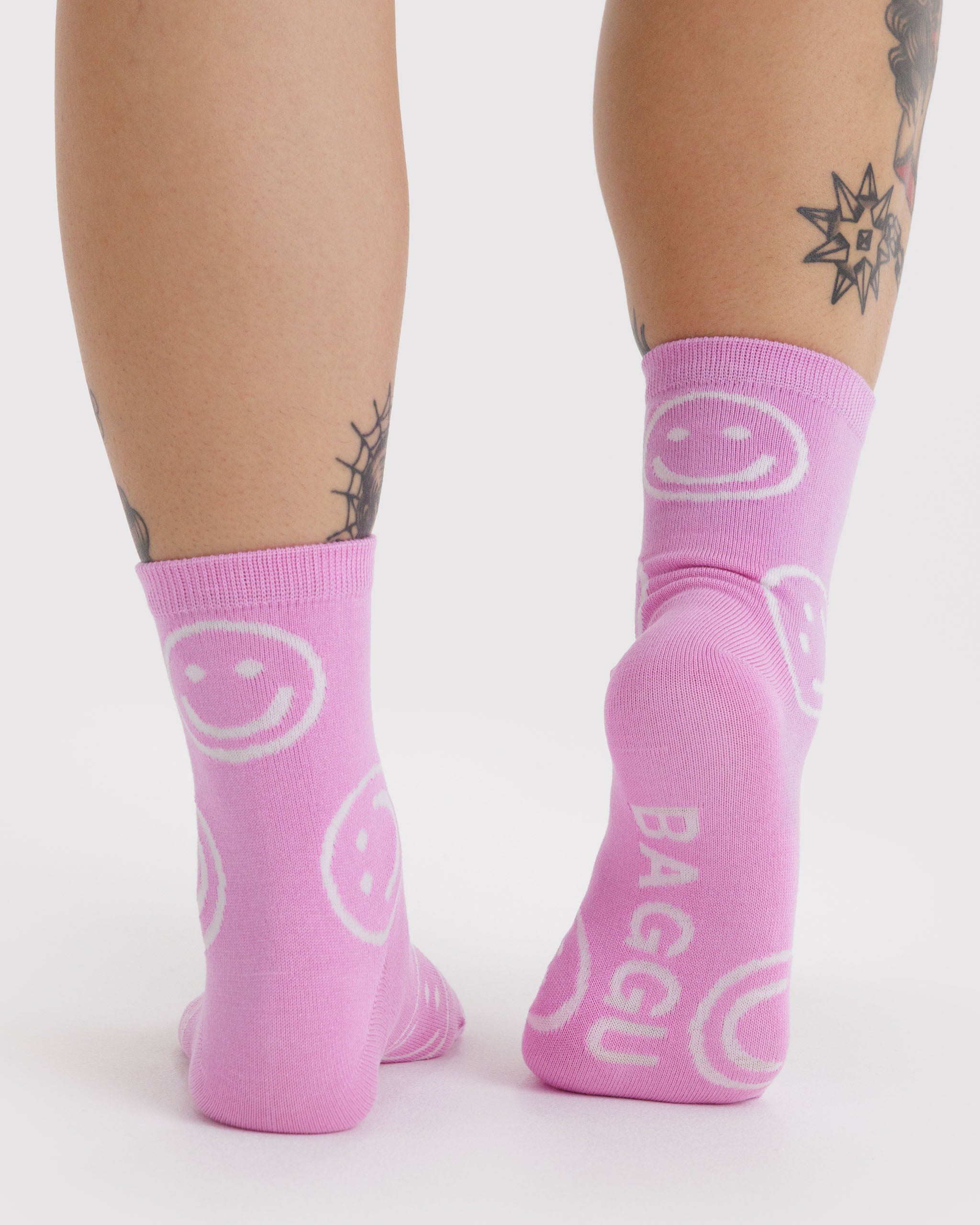 Person wearing pink socks with smiley face design and 'Baggu' branding on sole.