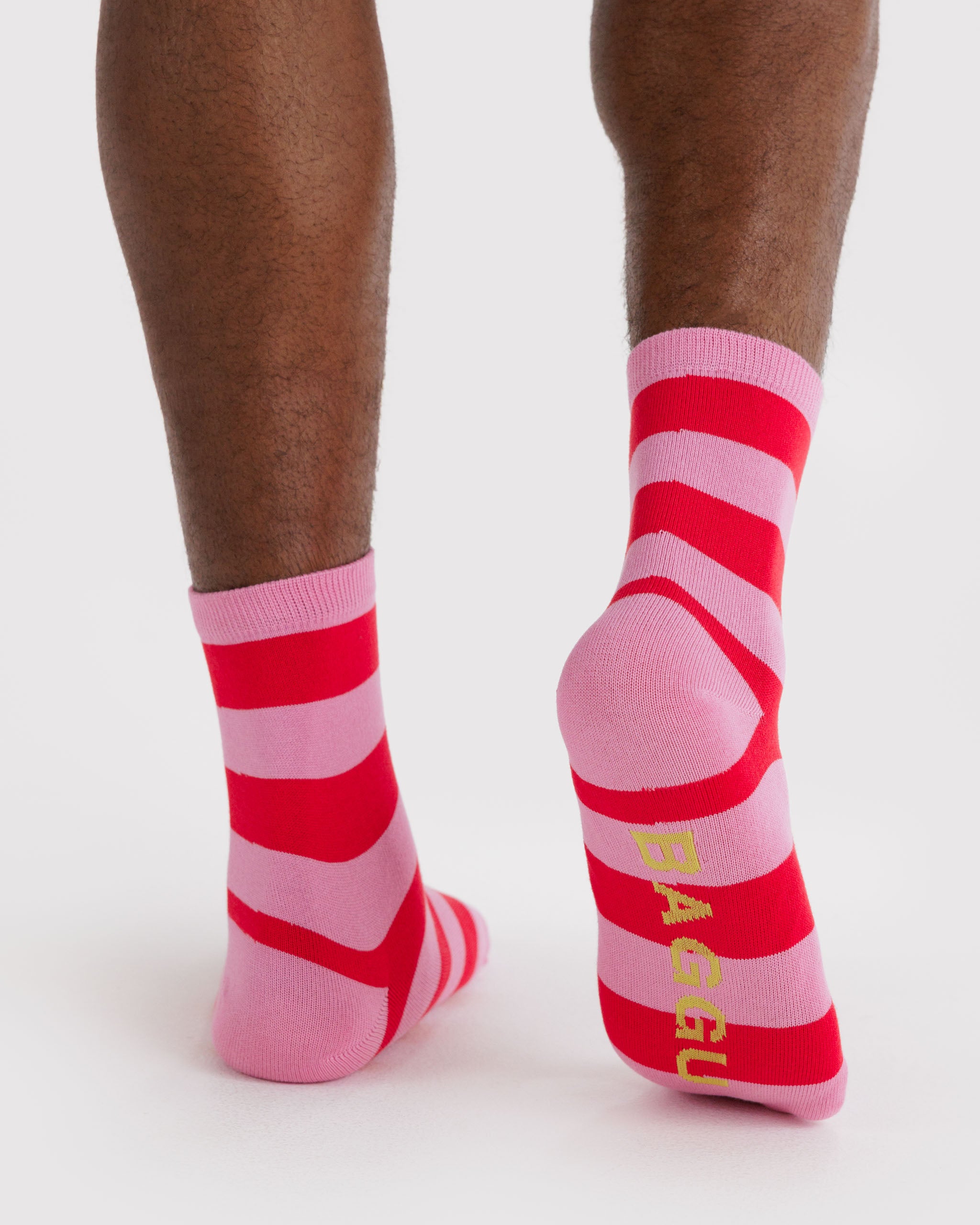 Person wearing a pair of pink and red striped socks with yellow 'BAGGU' branding on sole.